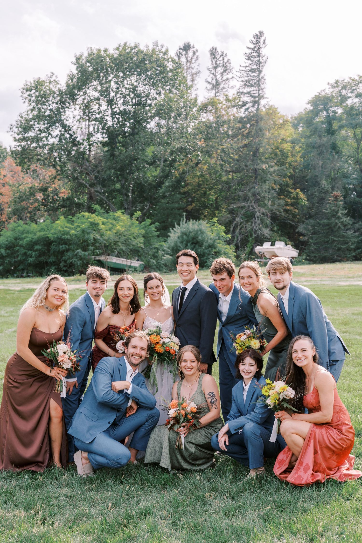 Wedding party poses together on grassy field with trees in background during autumn.