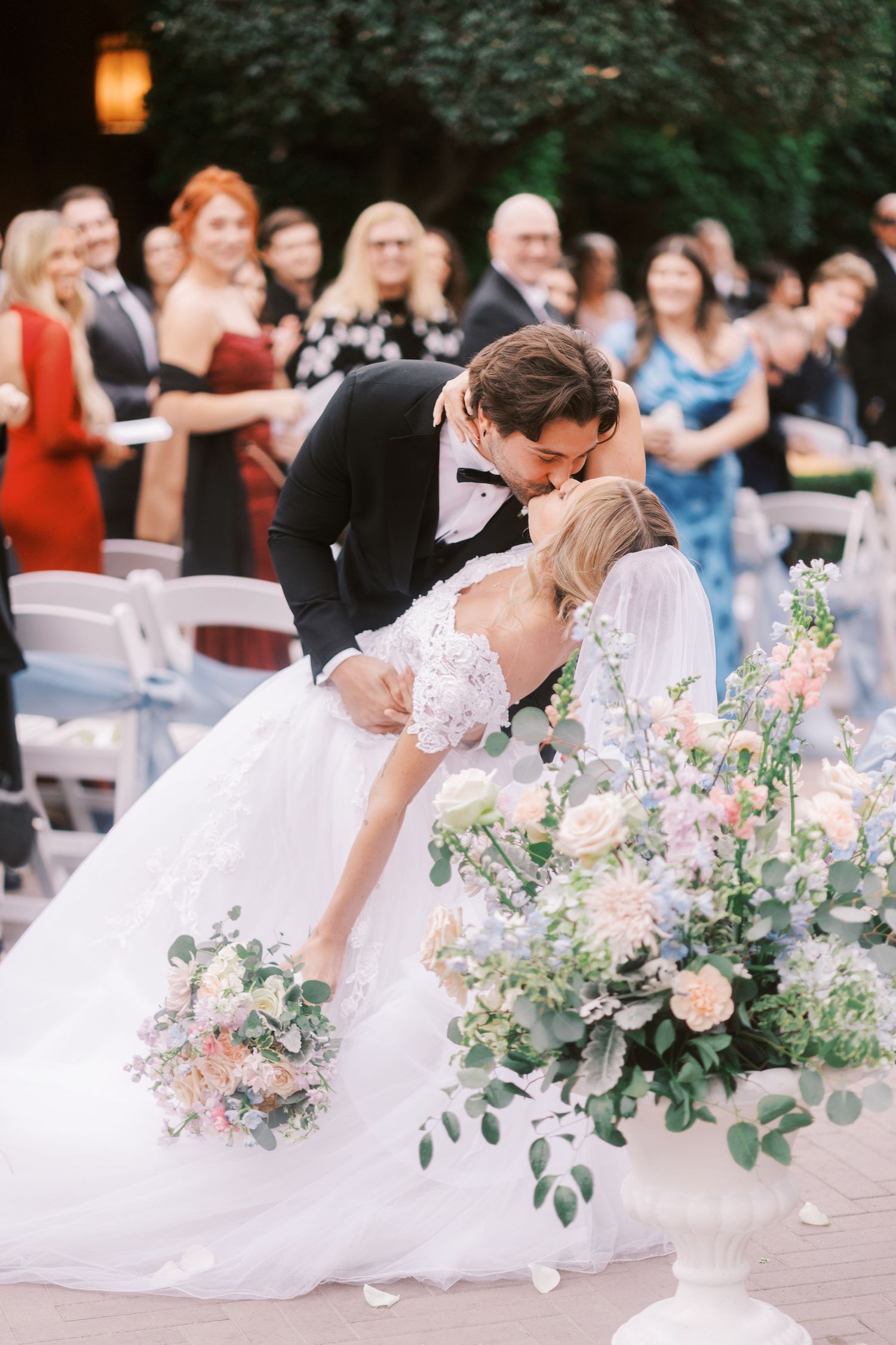 A romantic wedding sequence showing a couple sharing a tender kiss with floral arrangements and guests in the background.