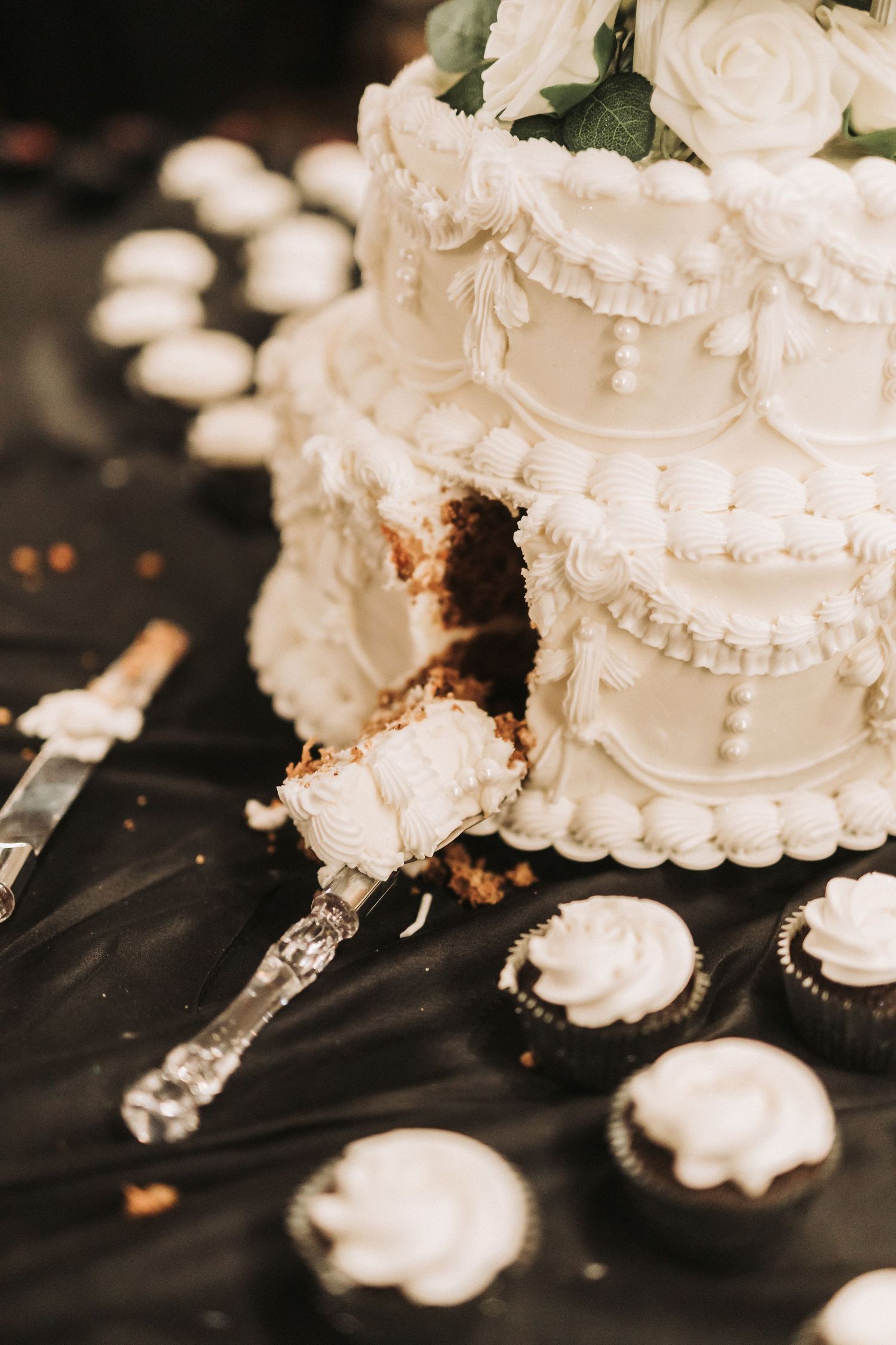 An elegant white wedding cake with ornate piping details and a slice being served with an antique silver cake server.
