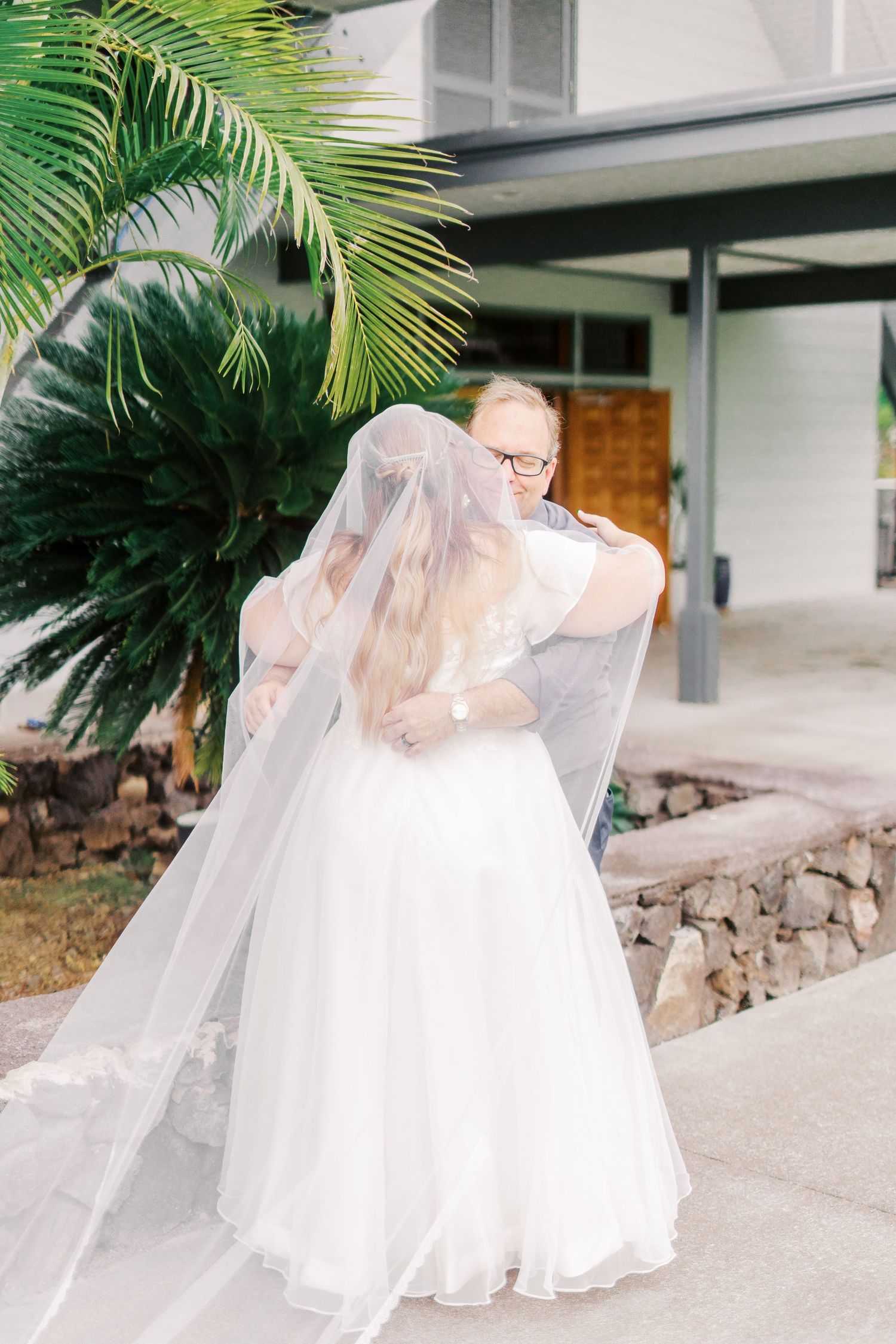 A series of candid wedding moments captured beneath tropical palm fronds outside a modern building.