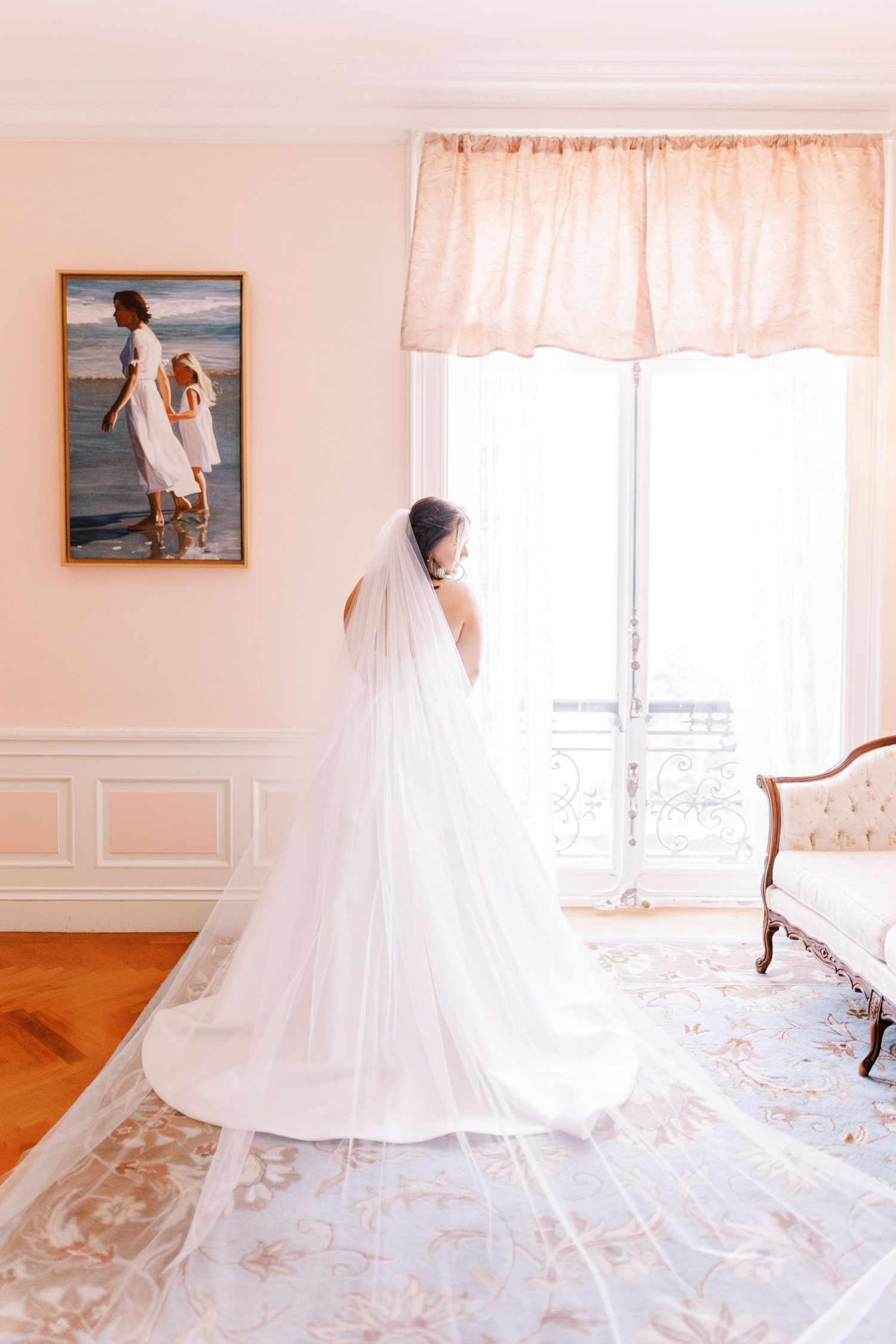 Elegant wedding dress with flowing train displayed in a sunlit room with hardwood floors and delicate decor.