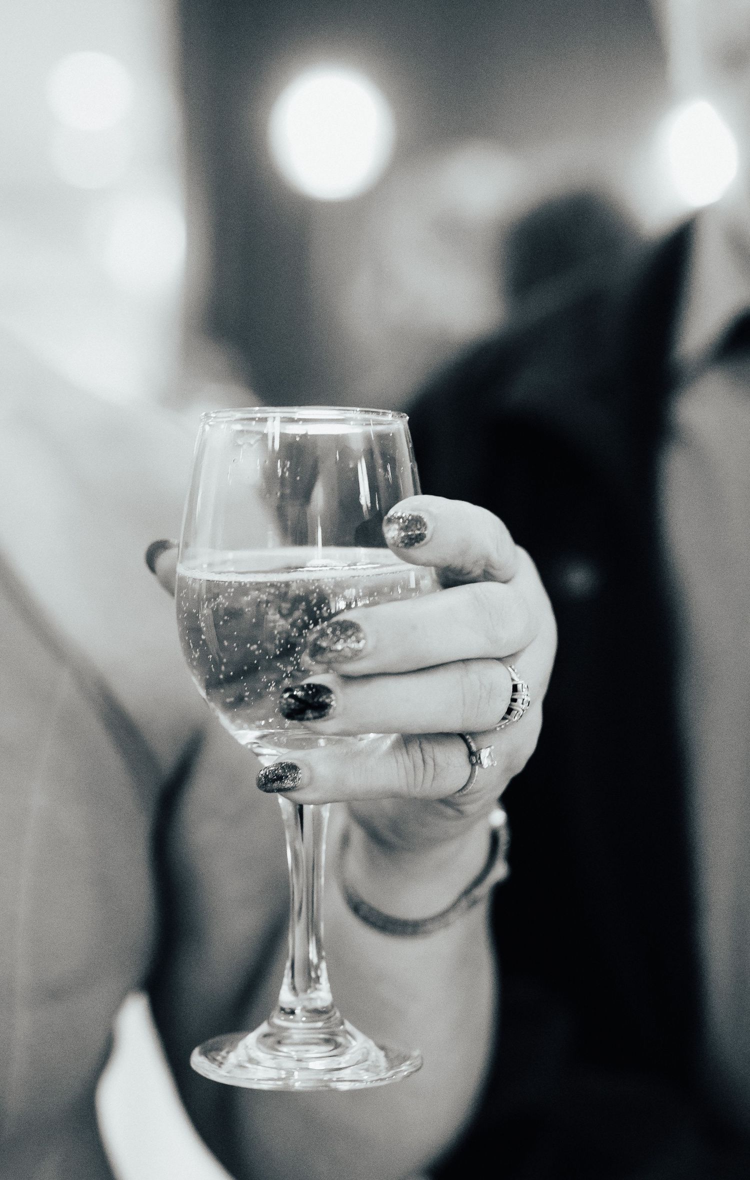 Black and white closeups of champagne glasses being held during a wedding celebration.