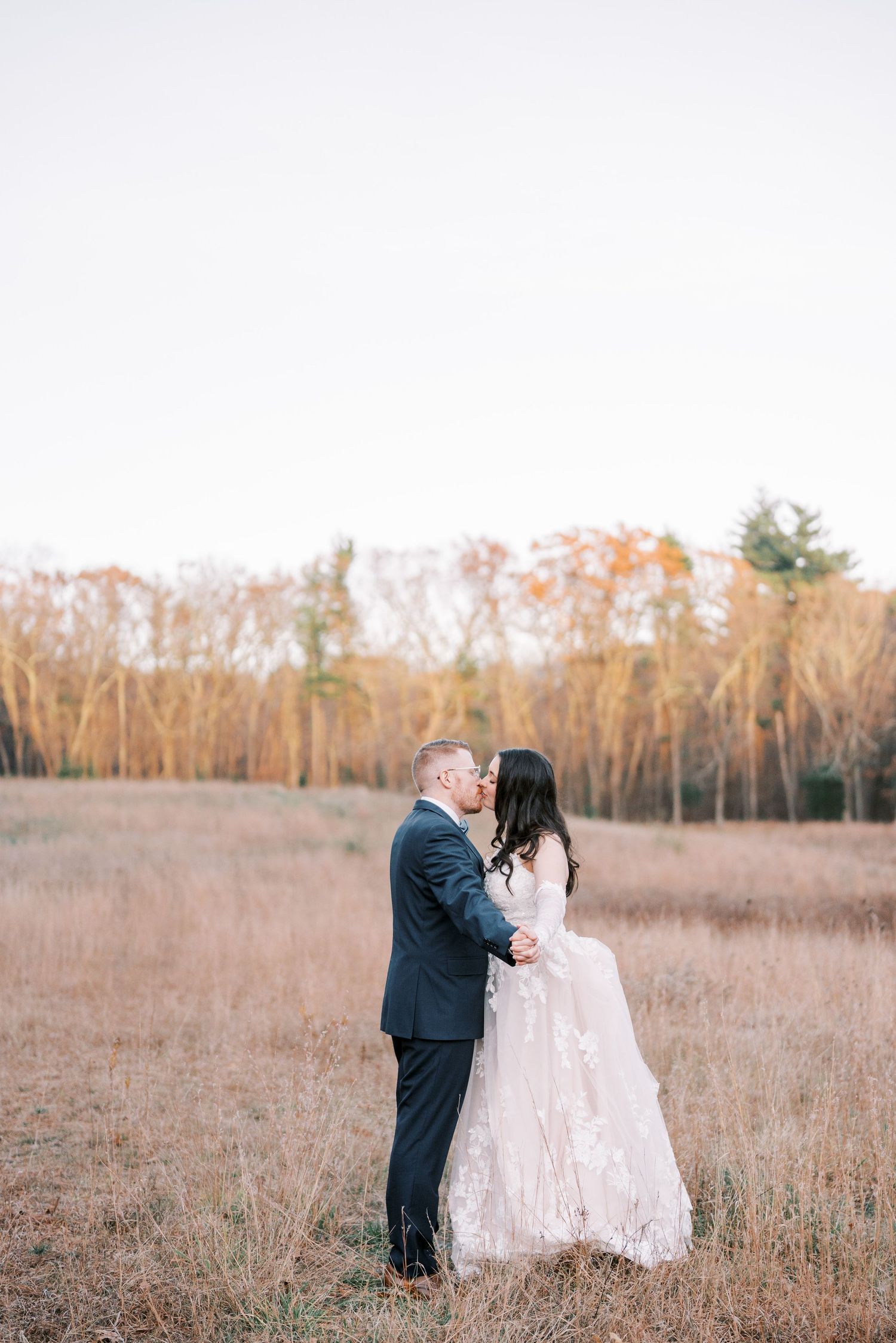 A couple in wedding attire shares an intimate moment in a golden autumn field during sunset.