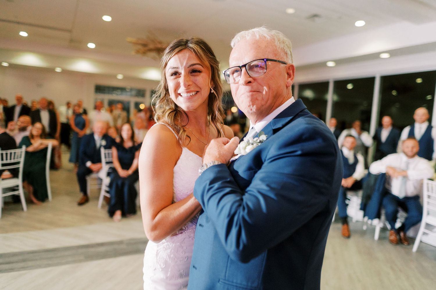 Wedding reception guests dance together in a bright indoor venue with recessed lighting.