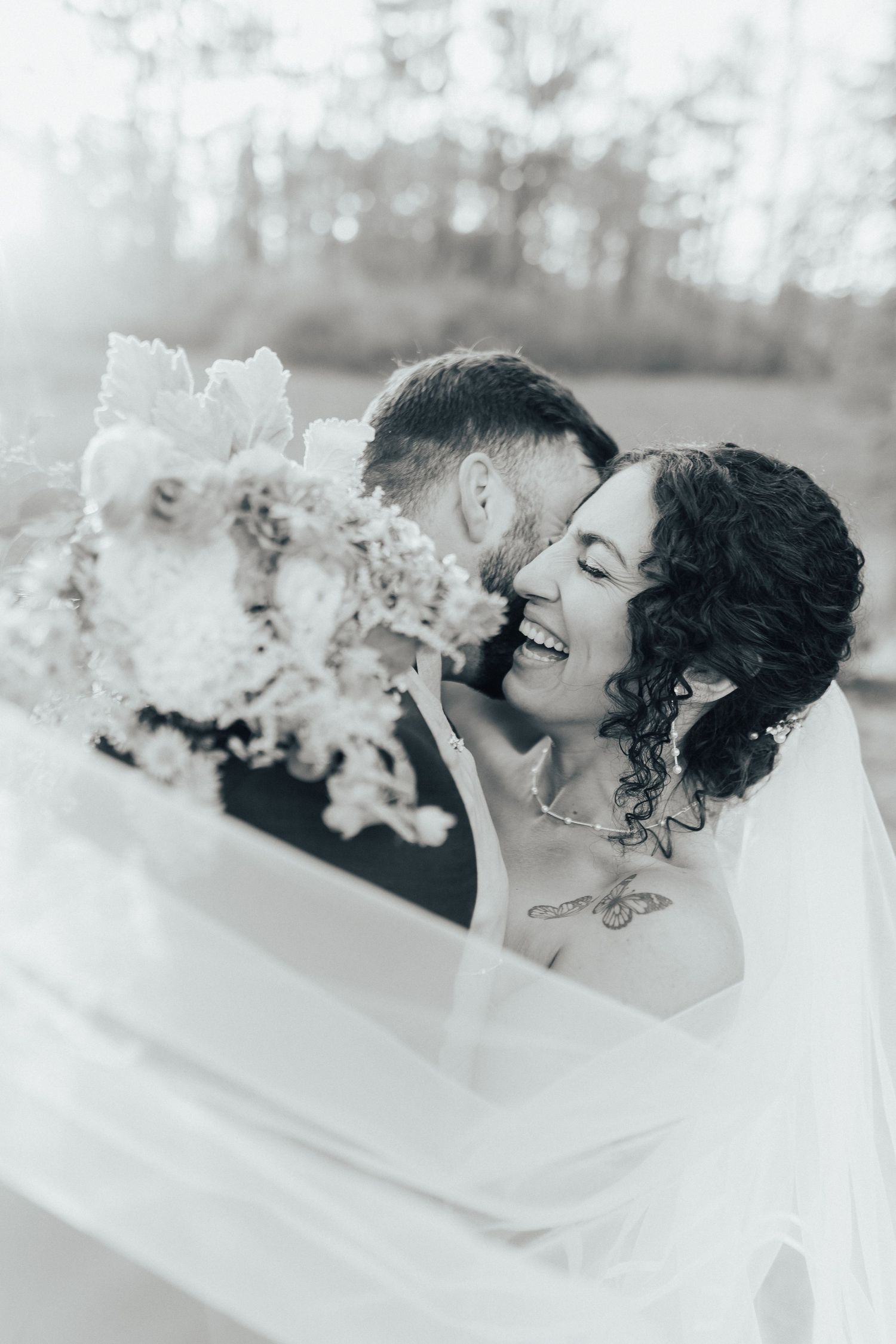 A couple shares an intimate kiss in a snowy winter landscape captured in black and white photography.