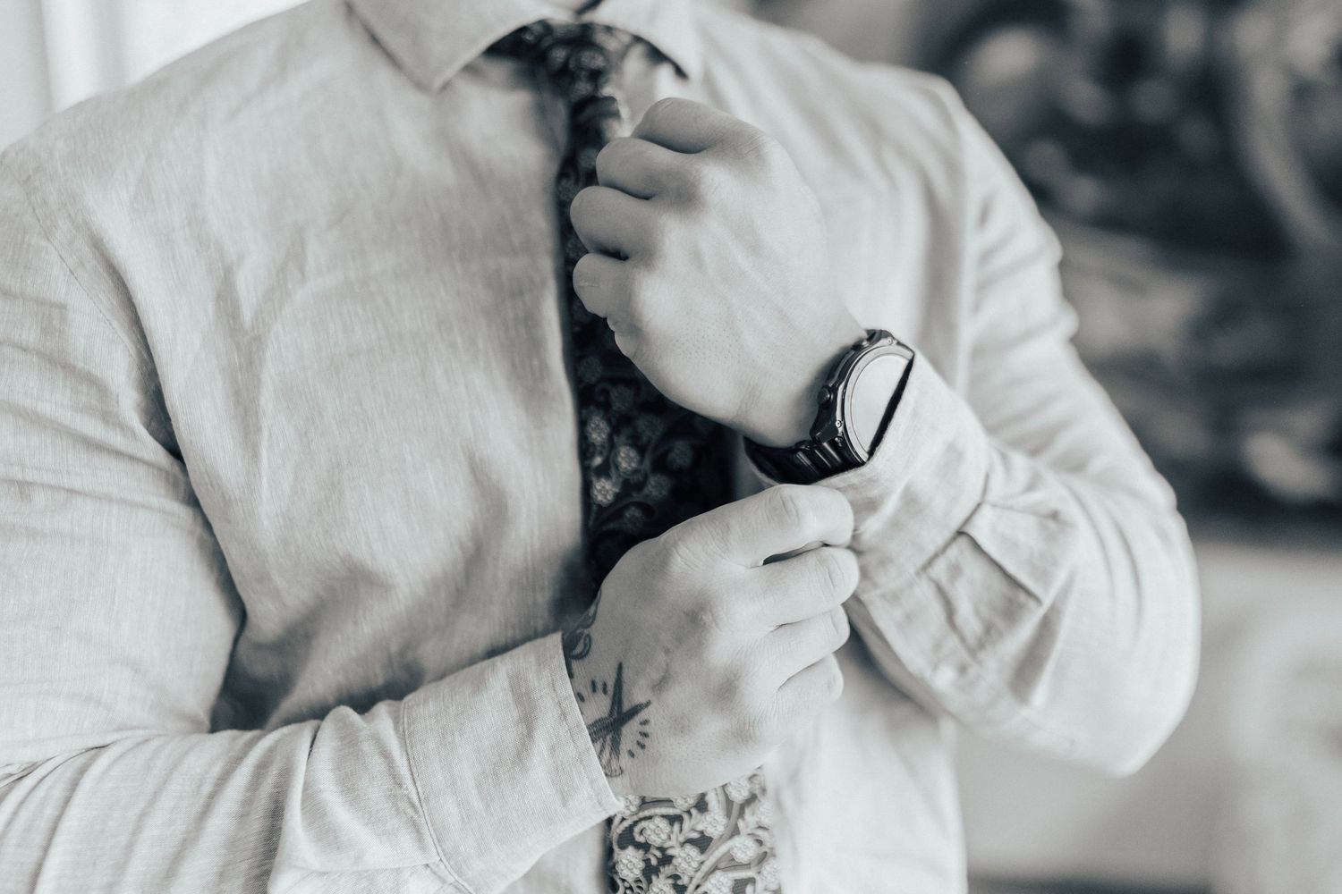 Close-up of hands adjusting a black tie while wearing a white dress shirt and wristwatch.