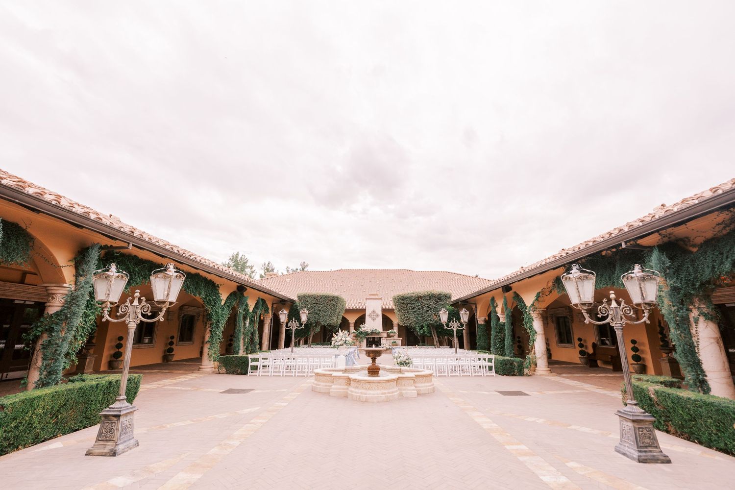 A panoramic view of a Spanish-style courtyard with terracotta tiles and decorative columns under an overcast sky.