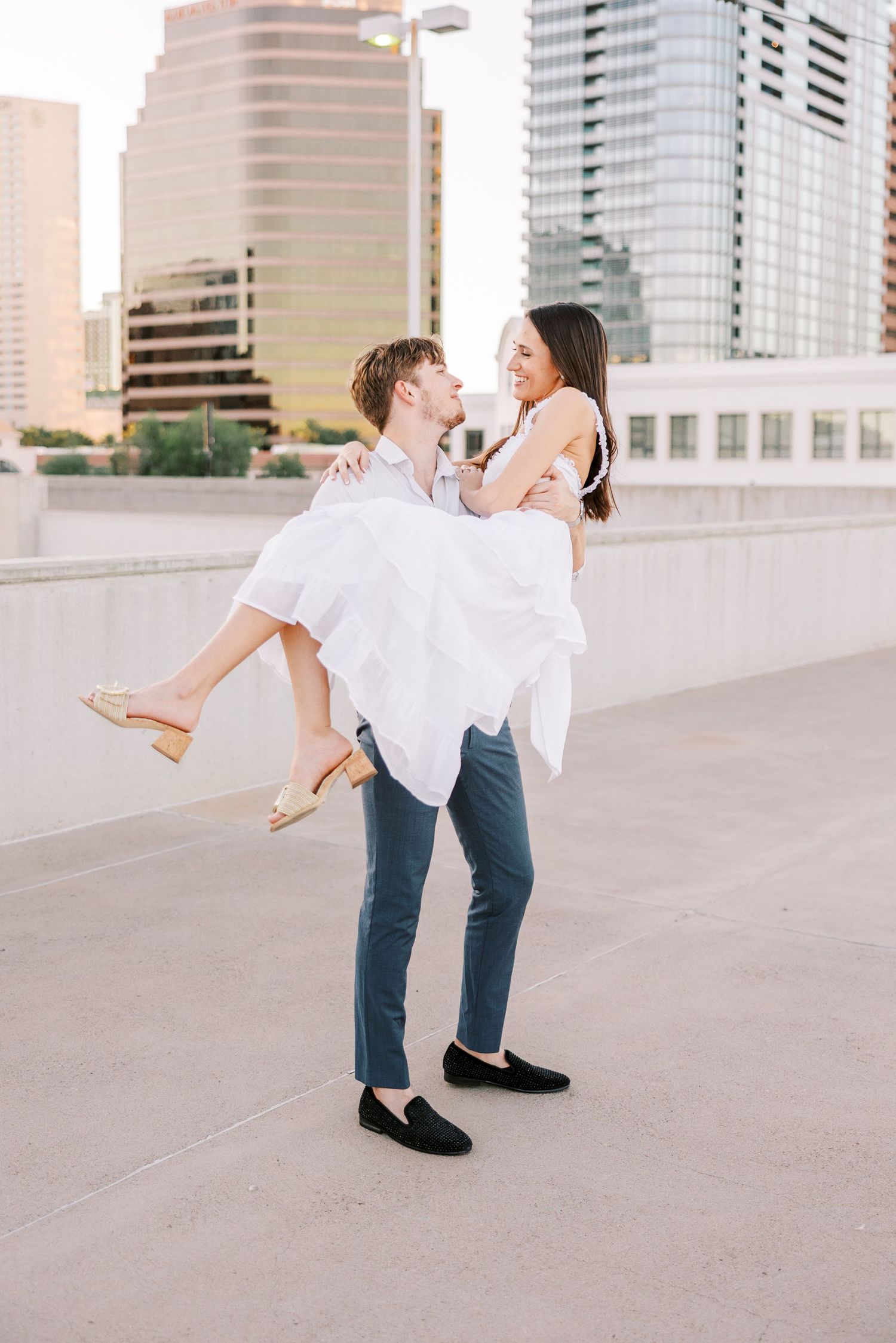 Couple in white and blue performing romantic lift pose against urban backdrop.