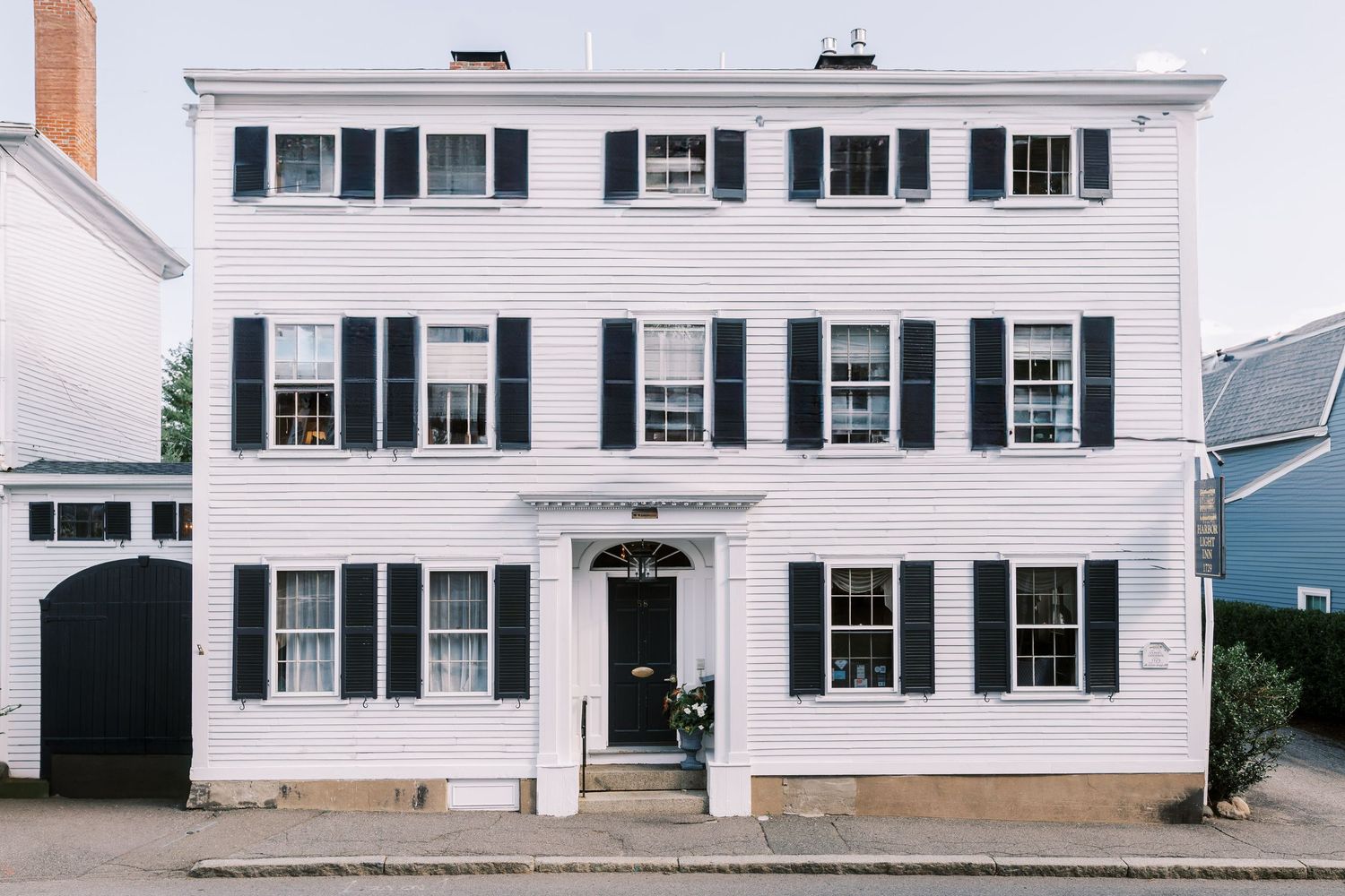 Classic white colonial house with black shutters and central door stands elegantly against blue sky.