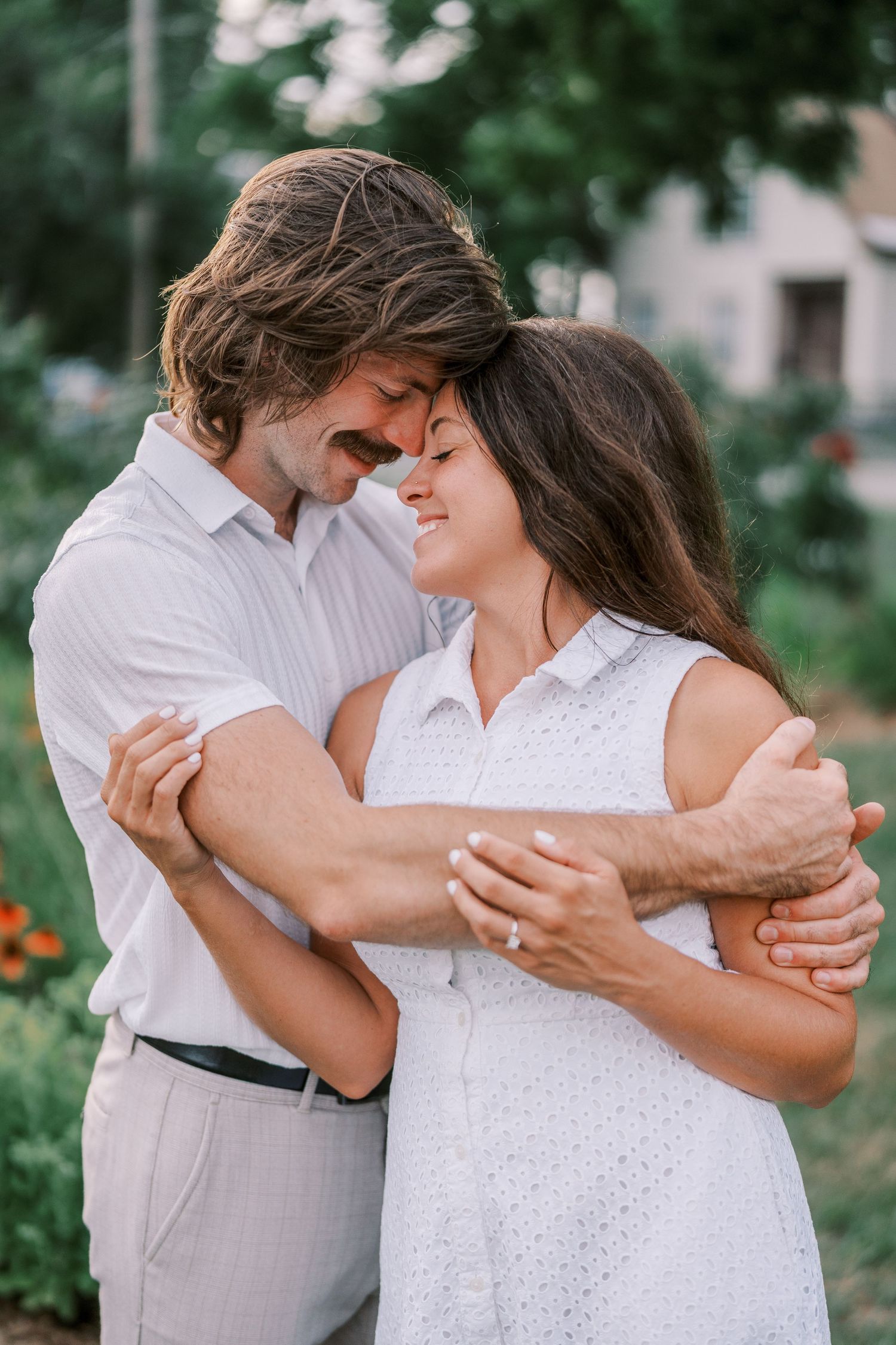 A couple dressed in white share tender moments and laughter while embracing outdoors.