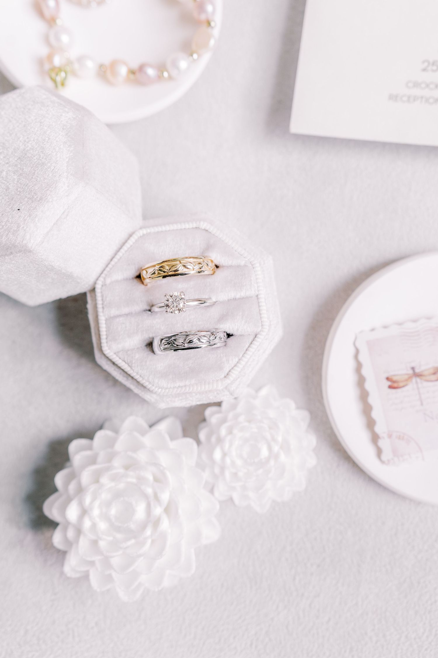 A delicate arrangement of white ceramic ring holders with floral designs displays elegant wedding rings on a light surface.