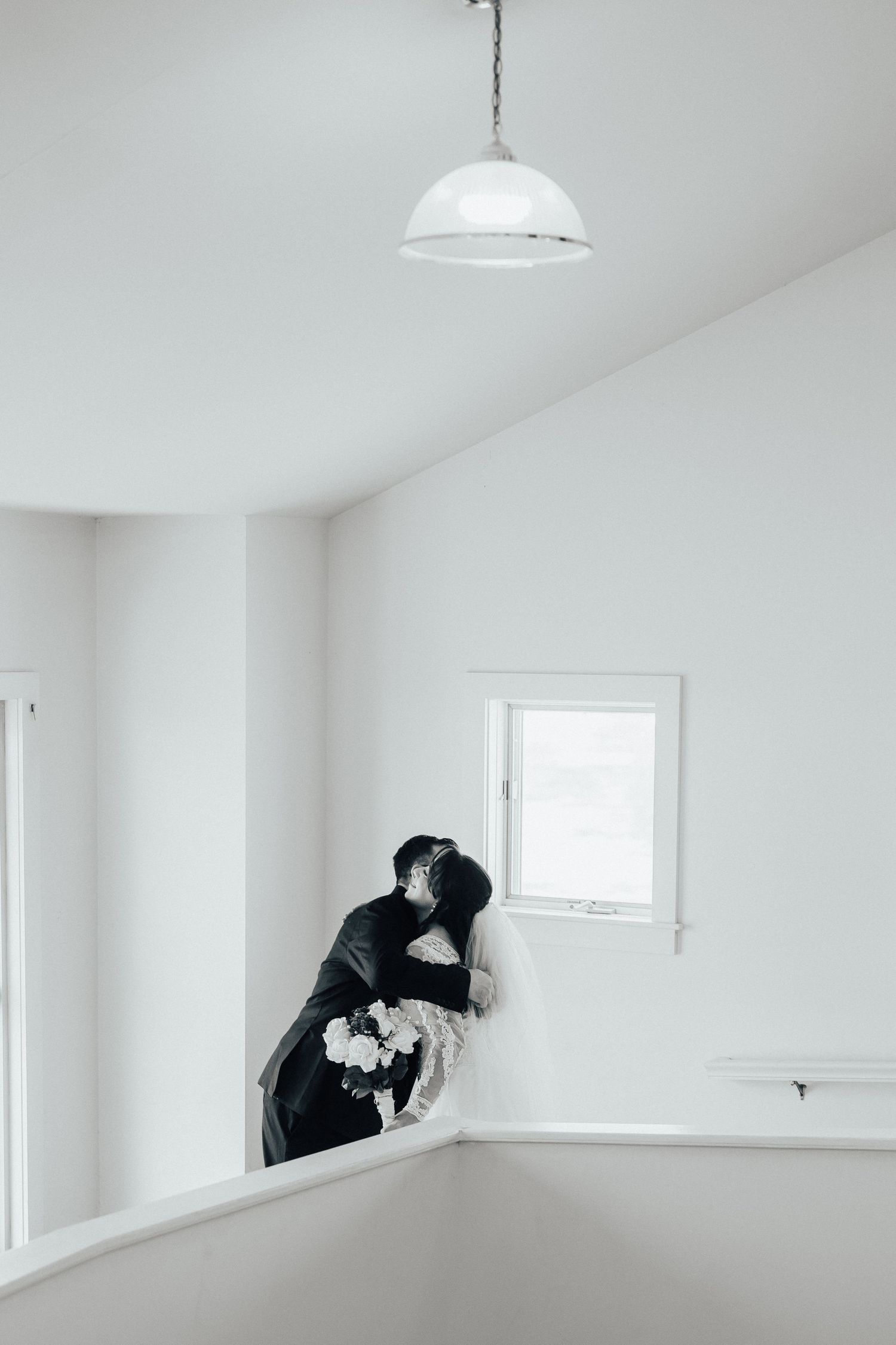 Artistic black and white photo of person in dark dress near window in minimalist white room.
