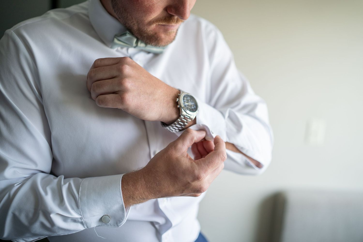 Someone wearing a white dress shirt adjusts their silver wristwatch while getting dressed.