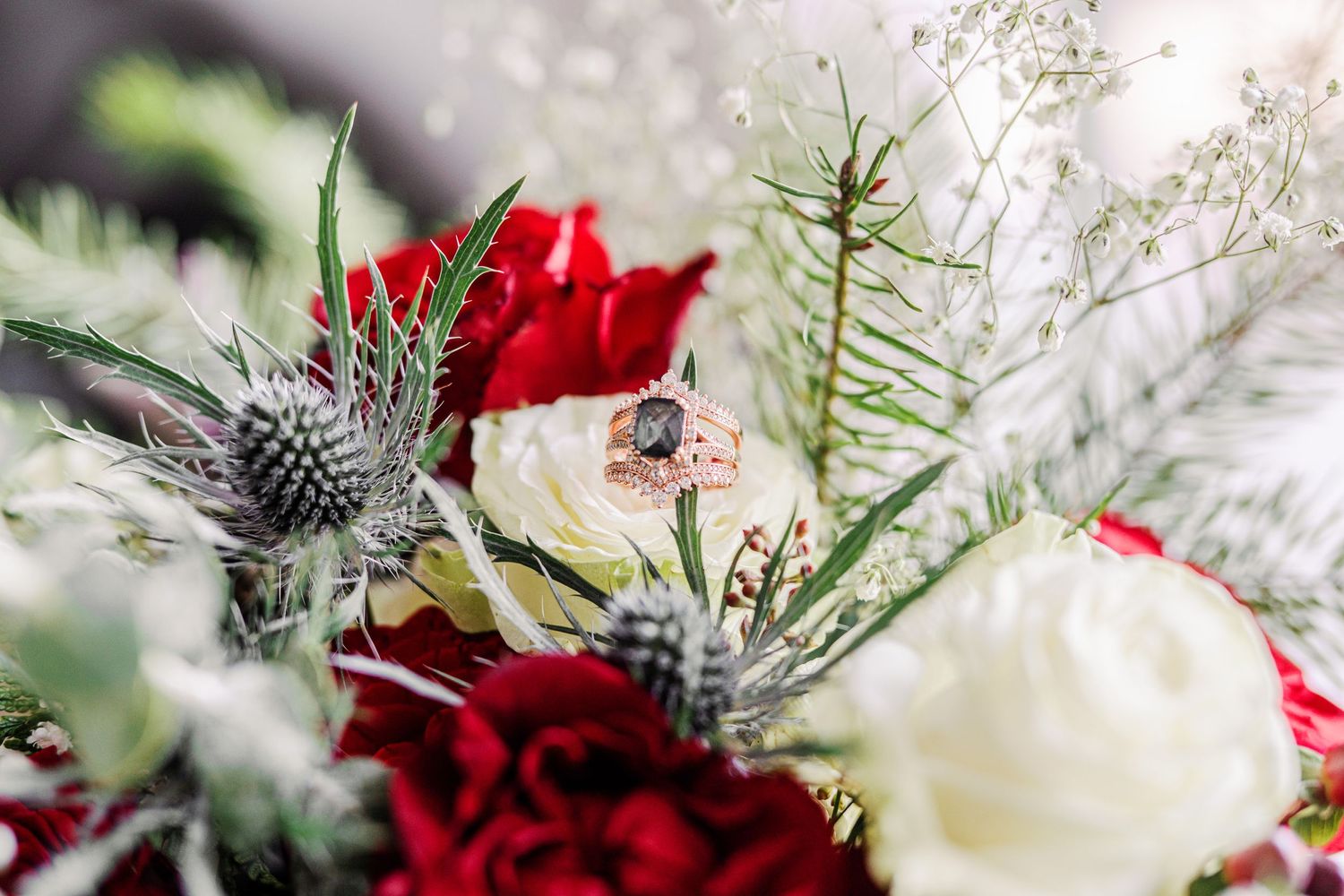 Close-up of a winter wedding bouquet featuring red and white roses with silvery thistle and evergreen accents.