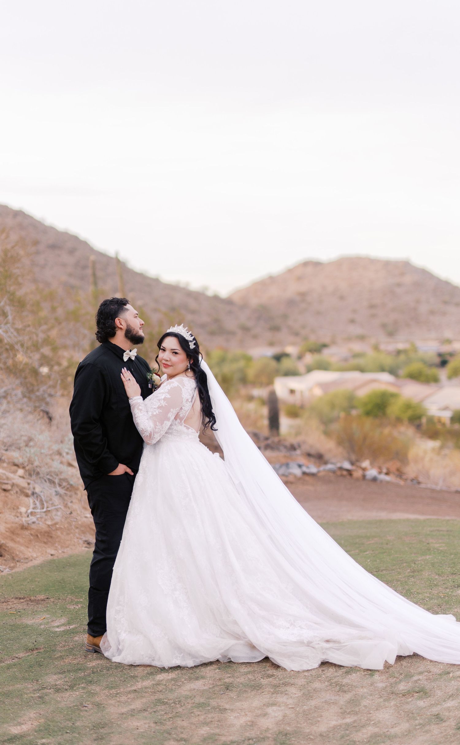 A wedding couple shares a romantic moment on a desert golf course with mountains in the background.