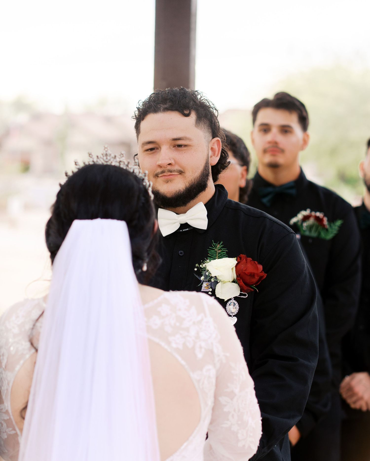 Wedding ceremony moment showing couple exchanging vows in front of floral arch with attendant watching nearby.