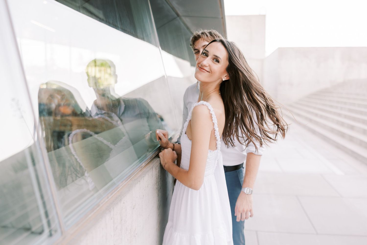 Couple in casual attire sharing a romantic moment against a modern architectural backdrop.