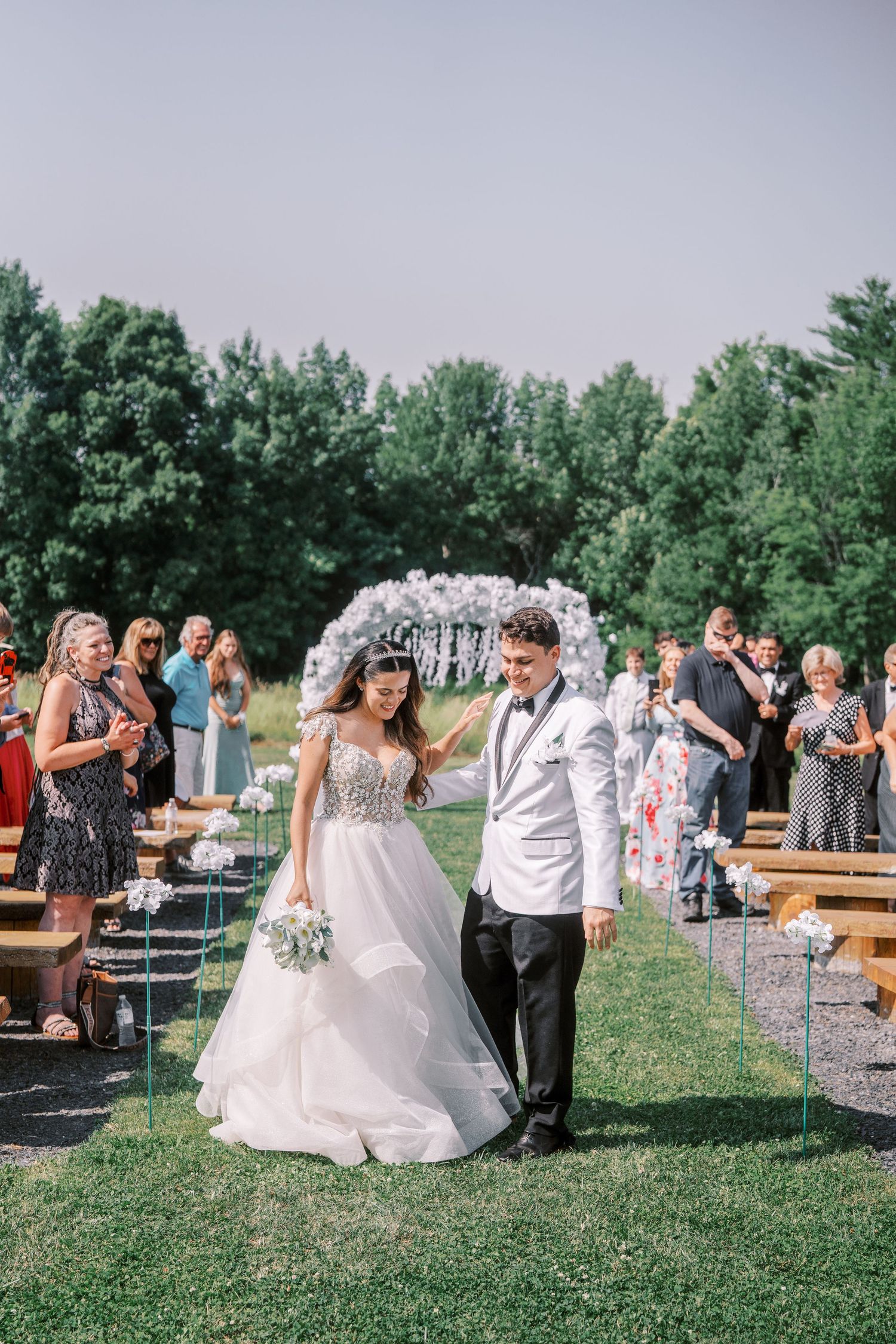 Wedding celebration at an outdoor venue with couples dancing on a grassy lawn surrounded by trees in the background.