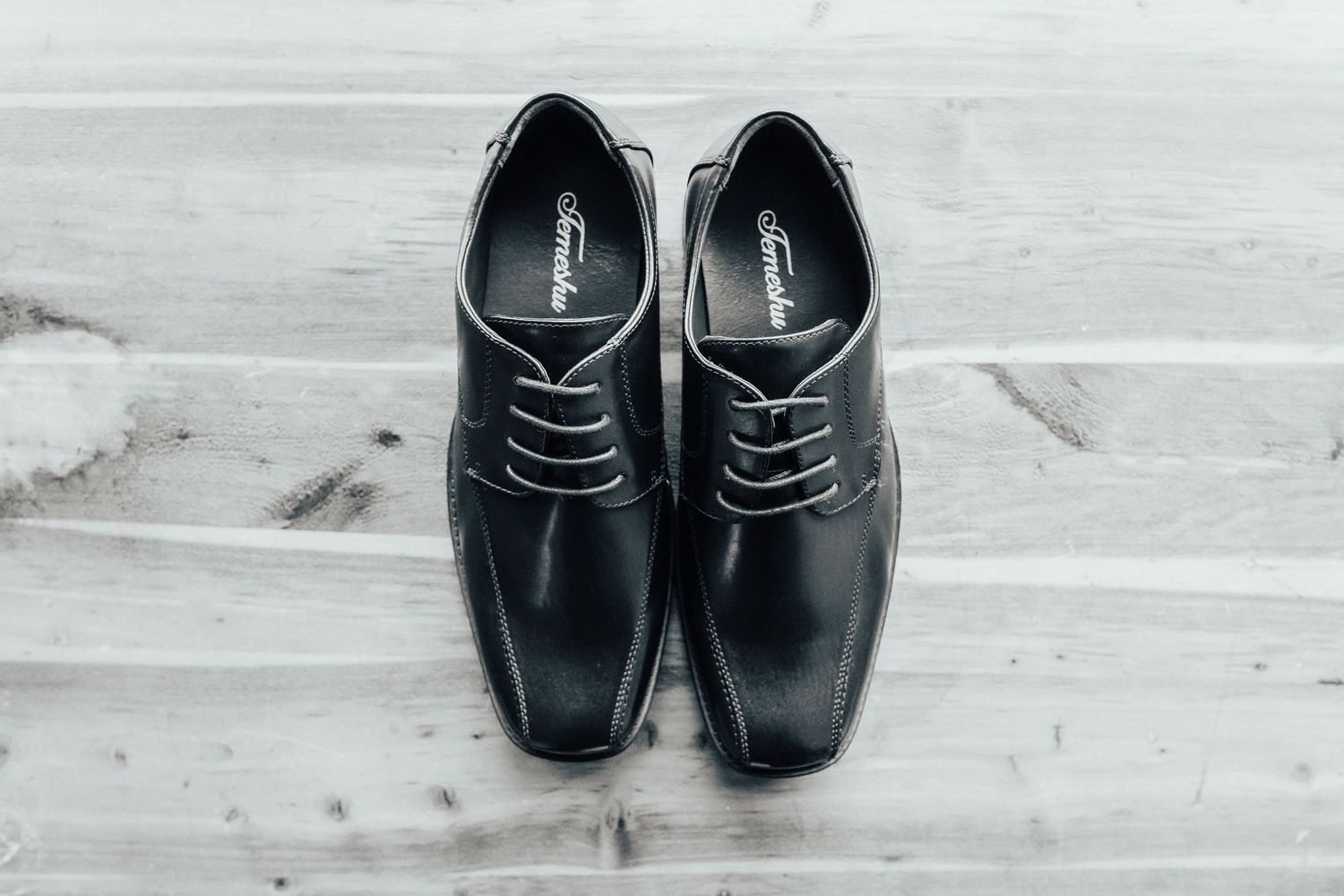 A sequence of black leather dress shoes arranged in a row on a light colored surface.