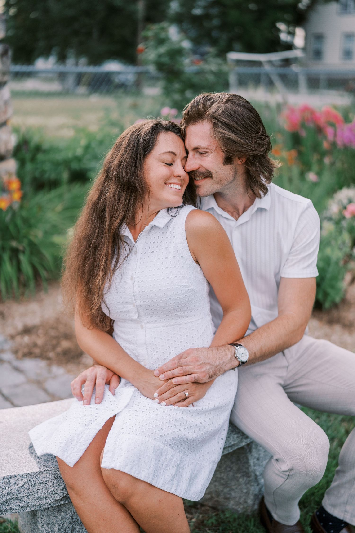 Couple shares tender moments while sitting in a blooming garden at sunset.