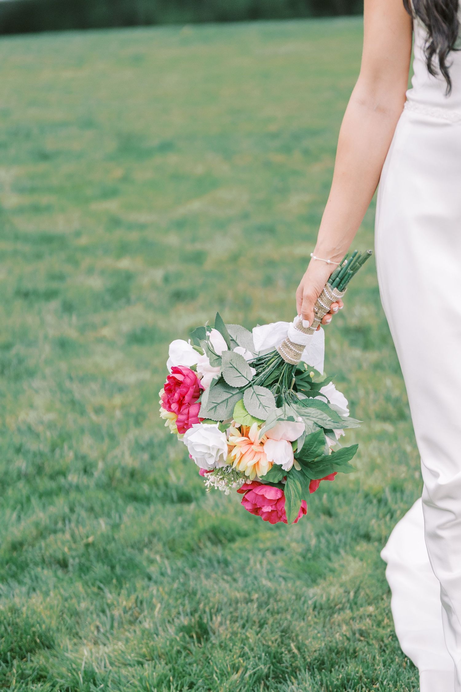 A cropped view of a wedding bouquet with pink and white flowers held against a white dress.