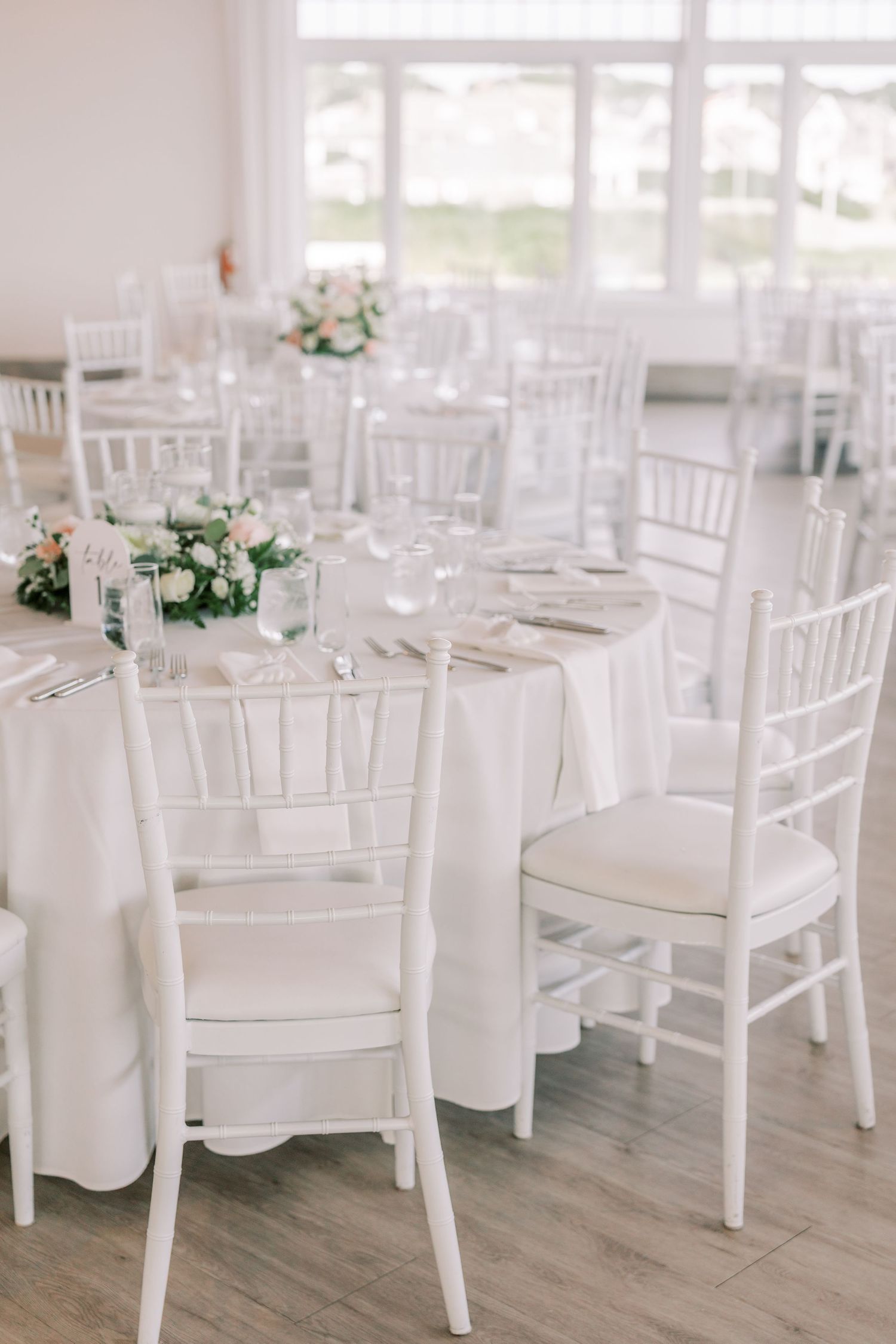 White chiavari chairs and round tables with white linens set up in an elegant wedding reception venue.
