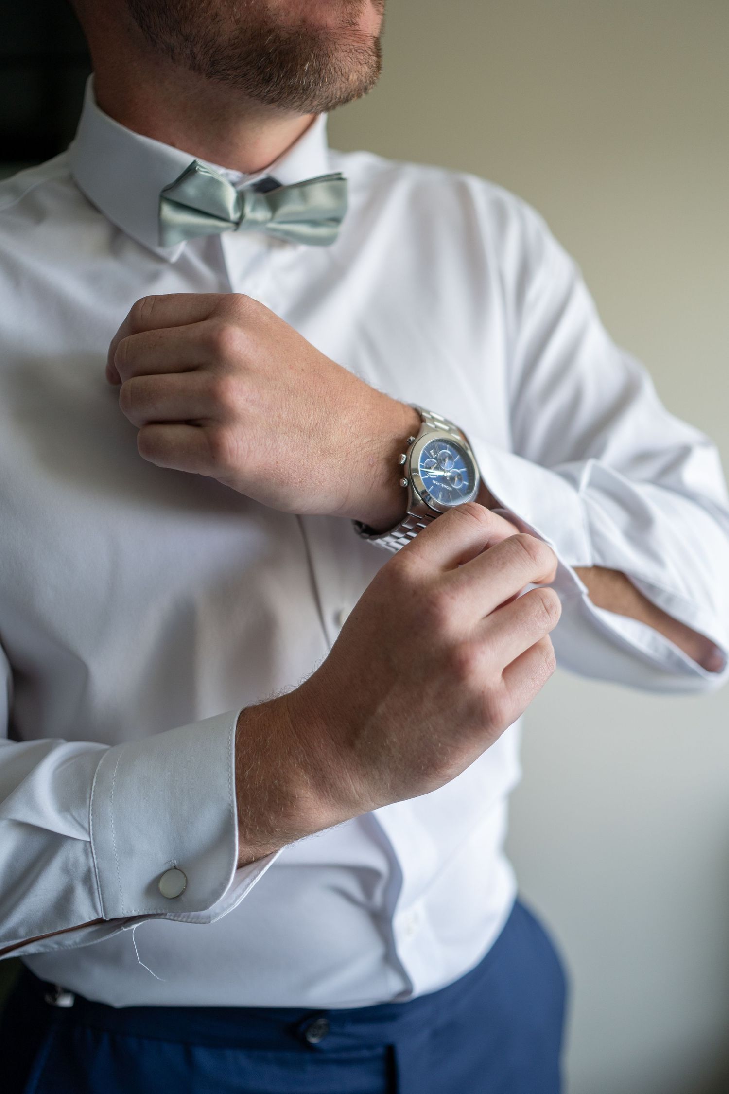 Close-up shots of someone adjusting a mint green bowtie while wearing a crisp white dress shirt and navy pants.