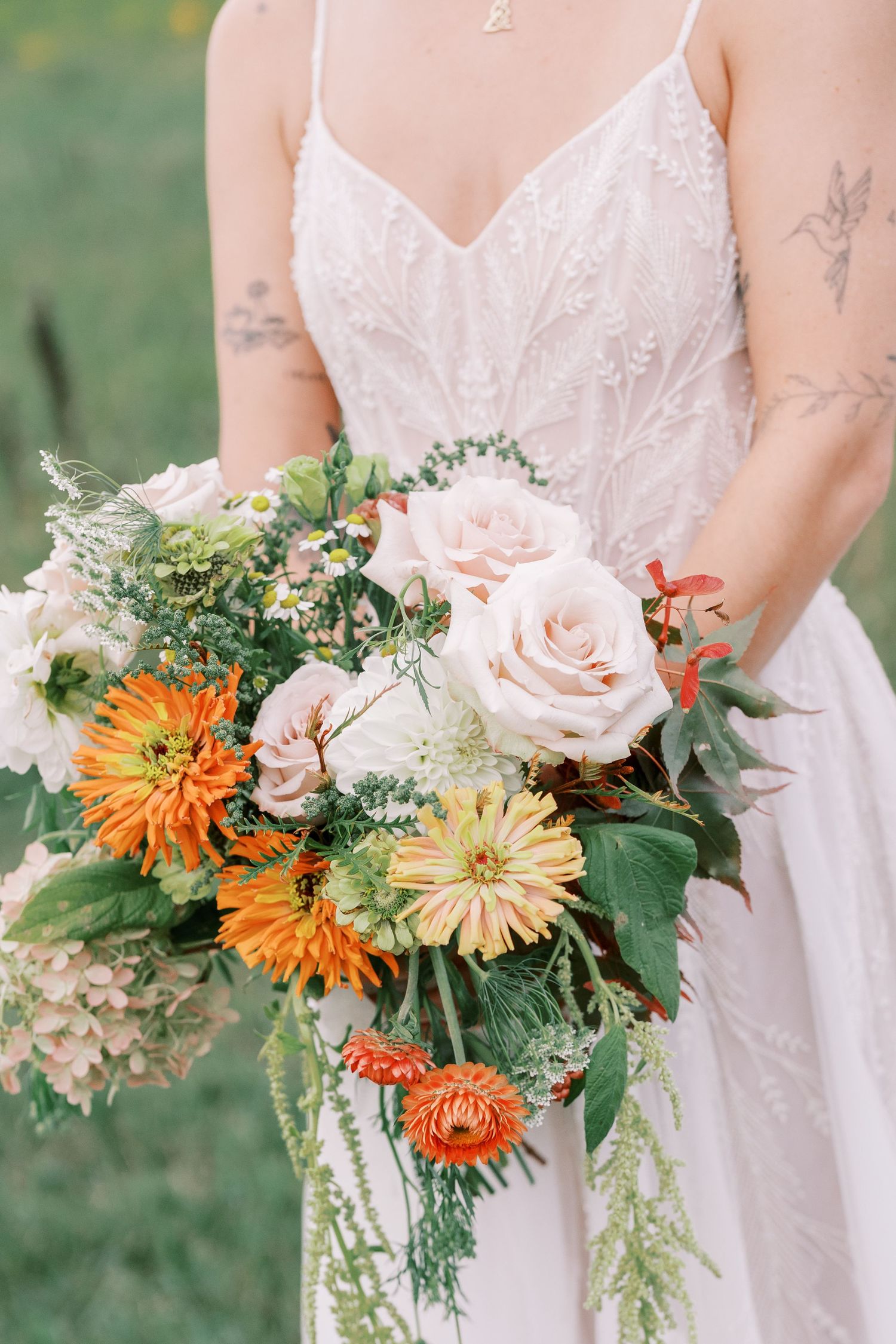 Close-up of orange and pink floral wedding bouquets with dahlias and roses against white dresses.