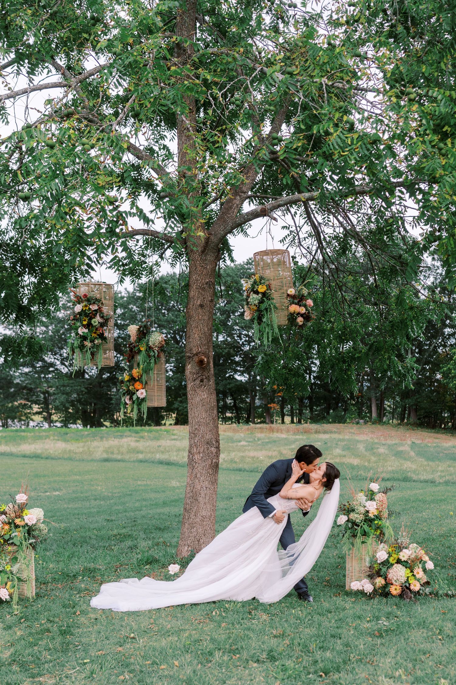 A romantic wedding couple shares intimate moments under a tree in a scenic outdoor setting.