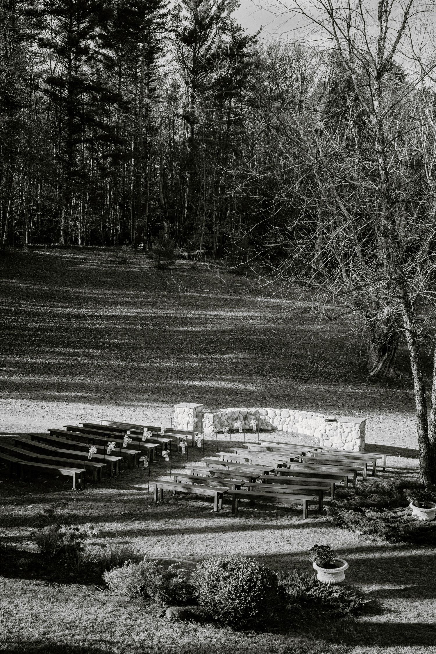 Black and white photo of an outdoor amphitheater with wooden benches surrounded by trees in a natural setting.