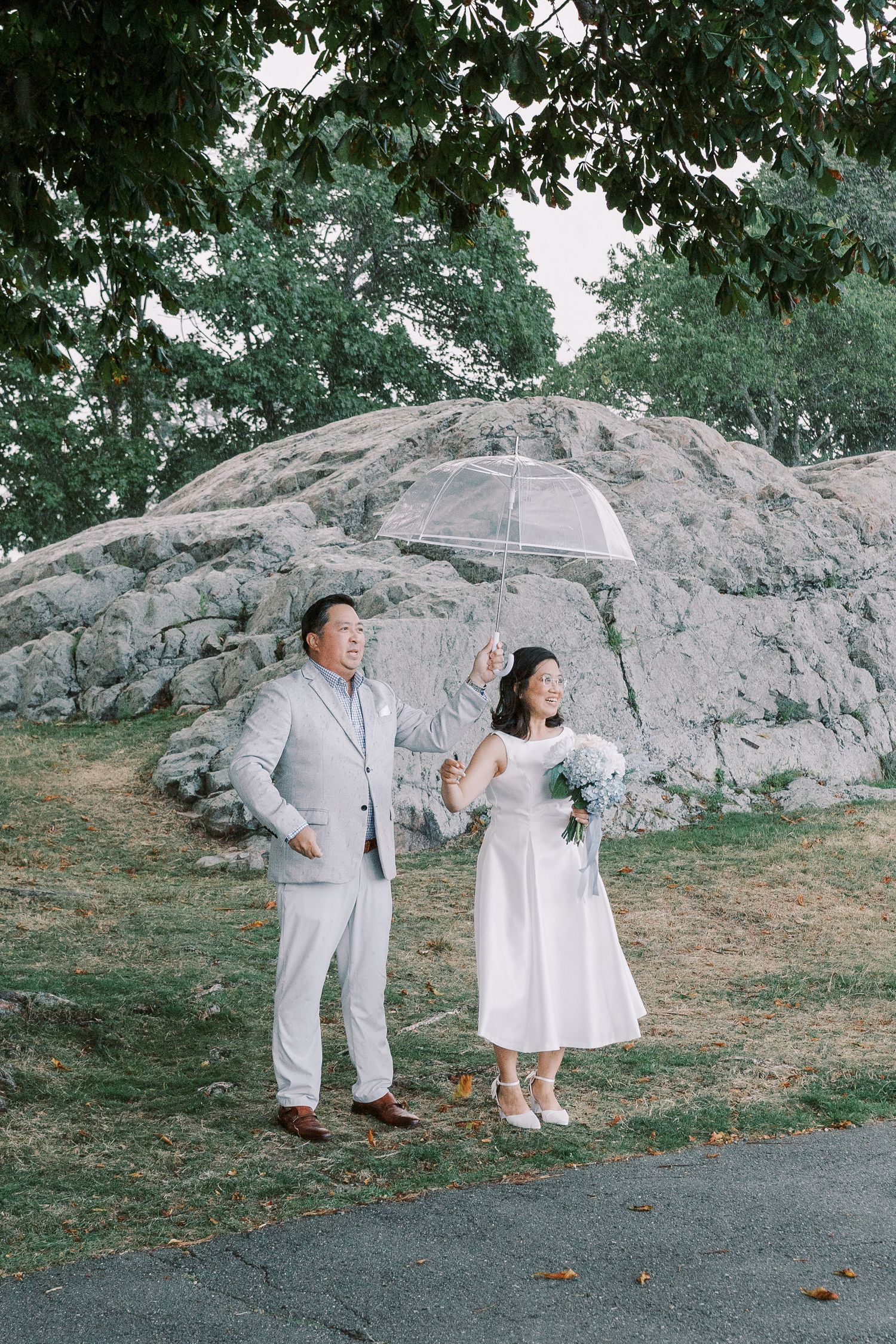 A couple poses playfully against a large rock formation in a scenic outdoor setting.