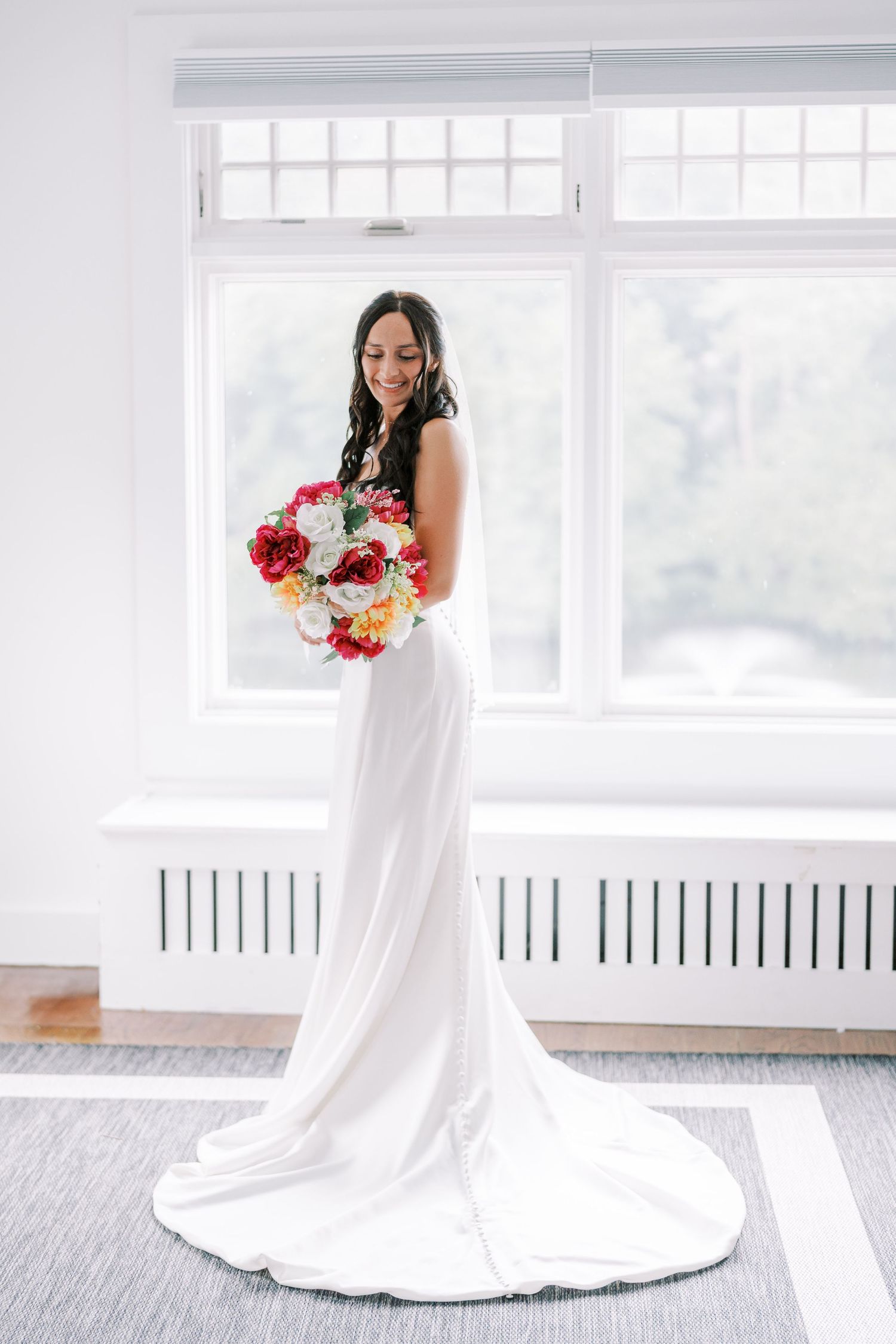 Elegant bridal portraits in a bright white room with floor-length gown and colorful bouquet.