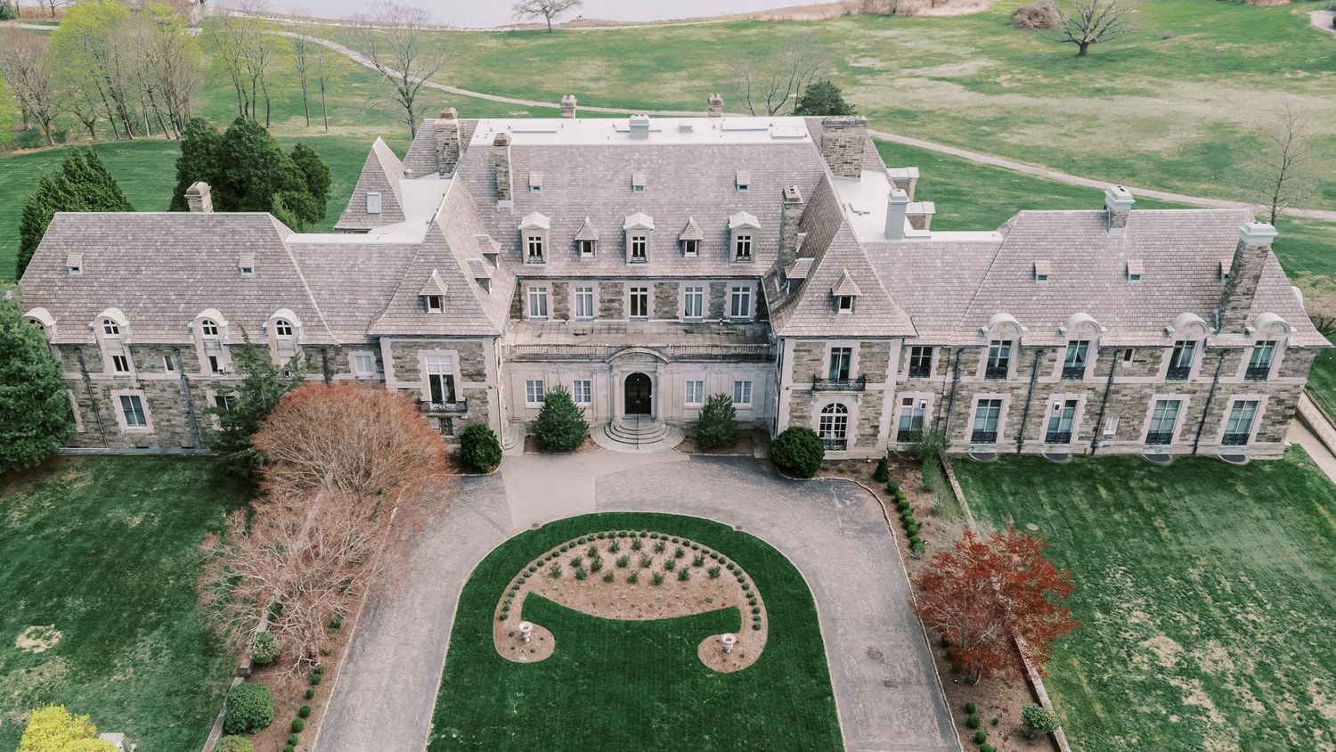 Aerial panoramic view of a historic stone mansion estate with manicured gardens and circular driveways.