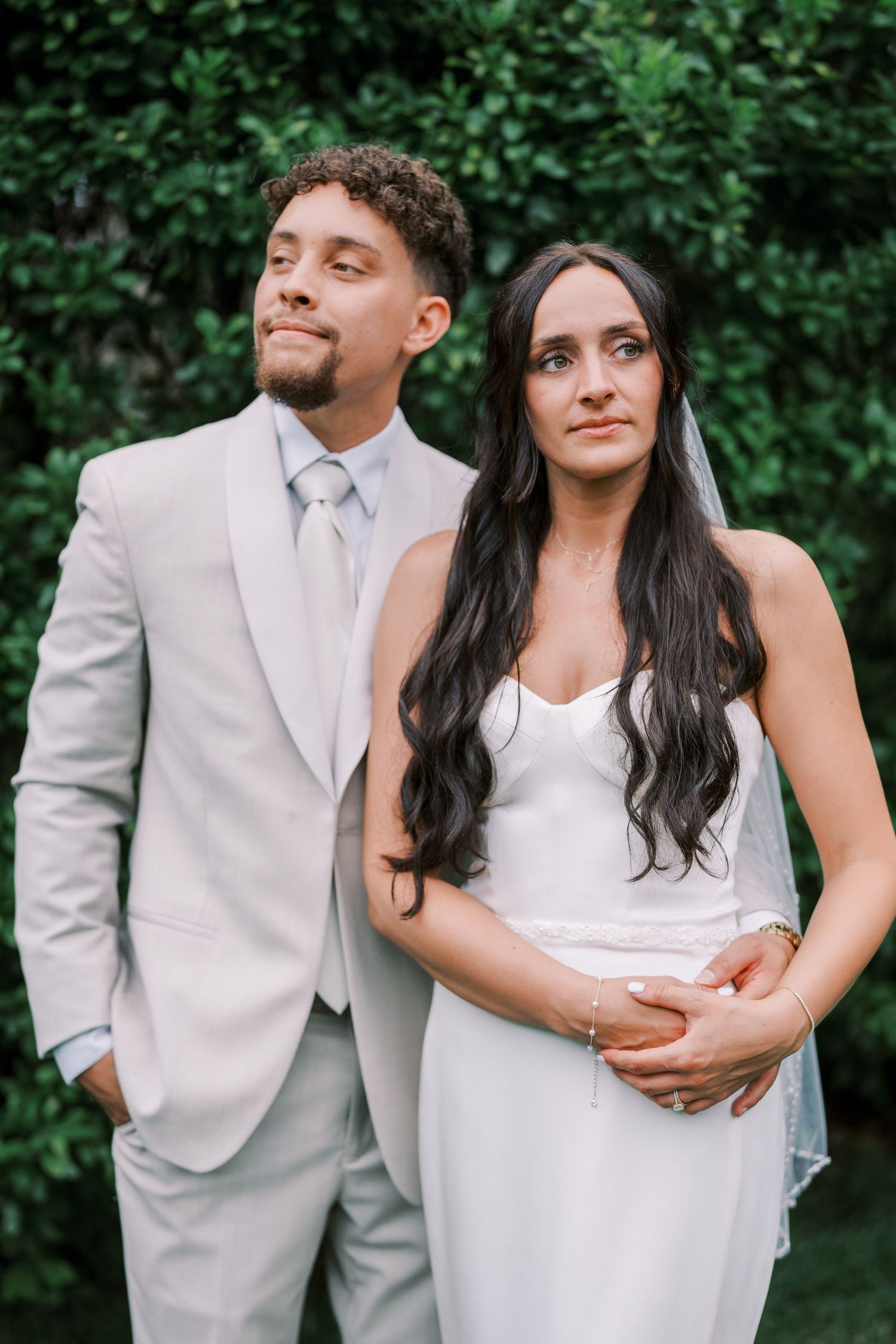 Happy couple in gray and white wedding attire pose playfully together in a lush garden setting.