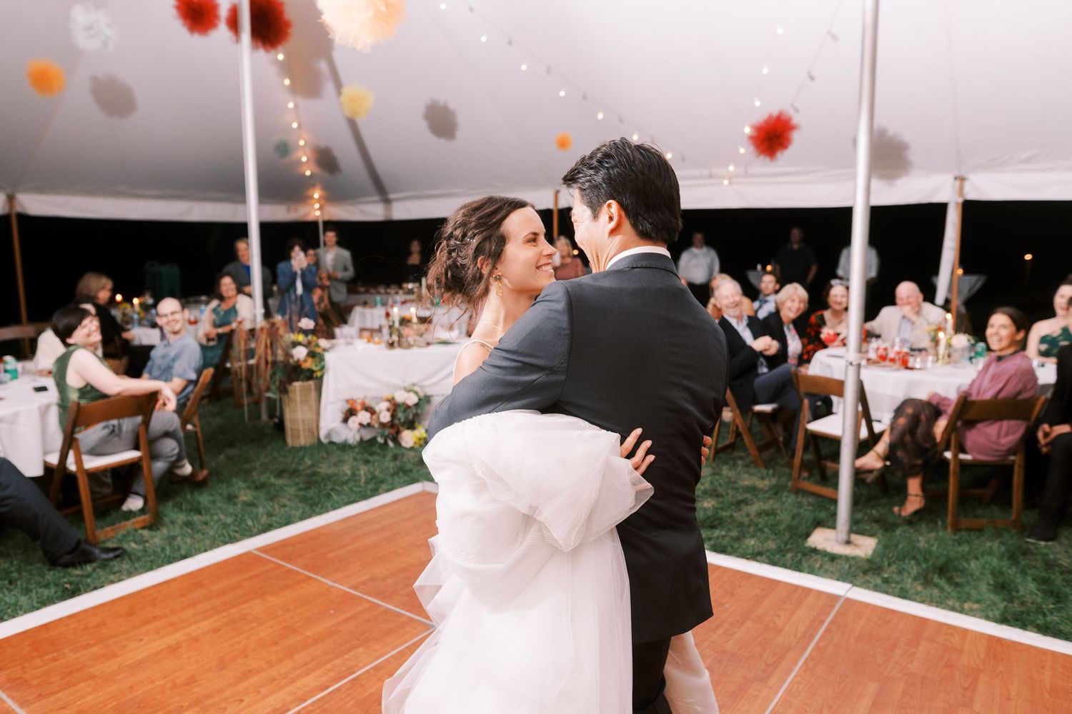 Wedding reception dance party in a tent with string lights and glowing lanterns creating a festive atmosphere.