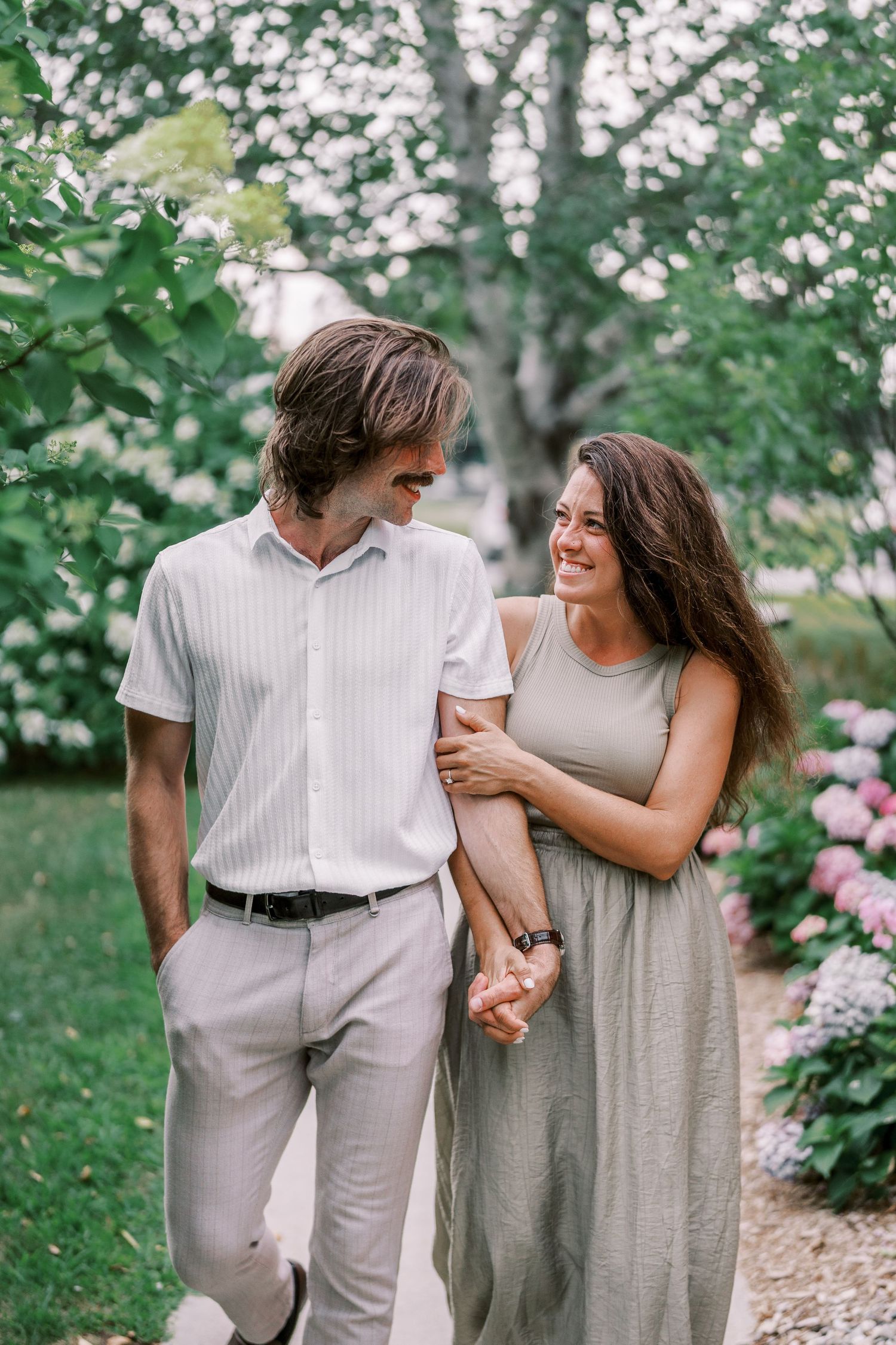 A couple shares intimate moments in a garden setting with pink flowers and greenery.