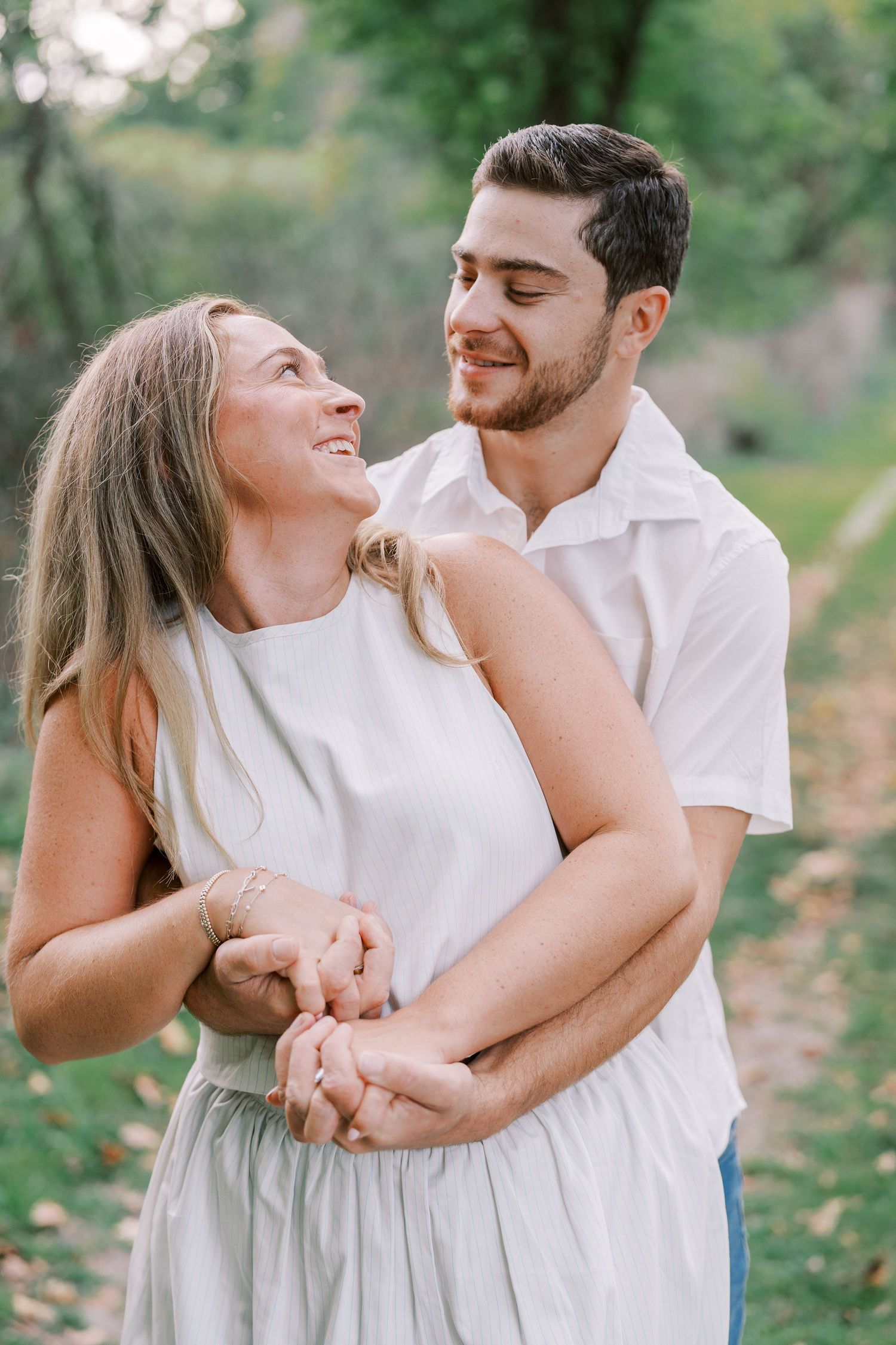 A couple dressed in white embracing and laughing together in a natural outdoor setting.