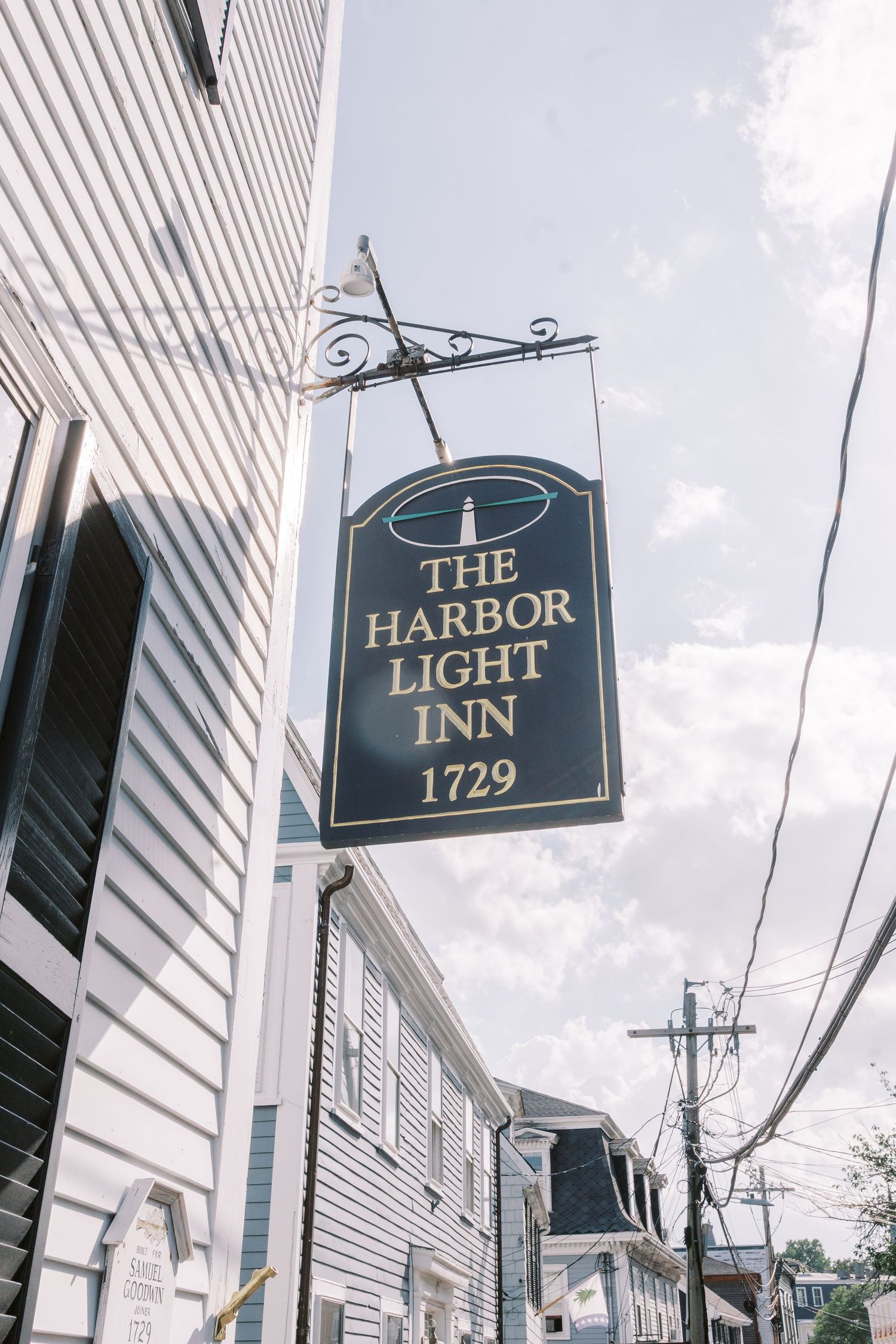 Classic New England inn signs including The Harbor and Light Inn 1729 mounted on white clapboard buildings.