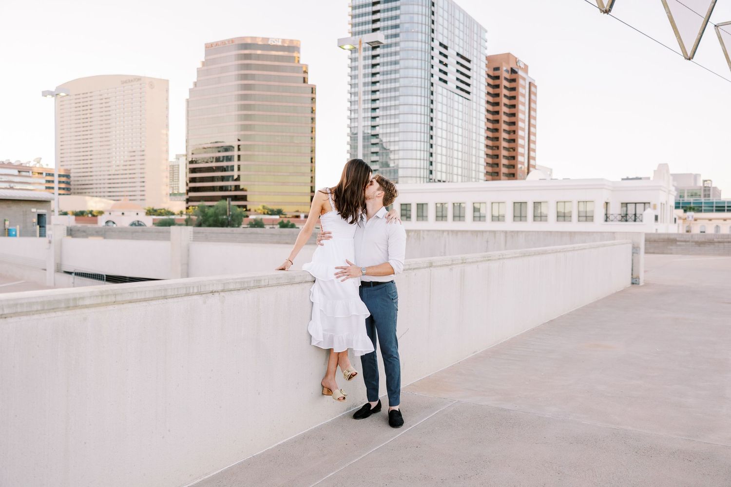 Two people in casual attire walk together on a modern rooftop terrace with city buildings in the background.