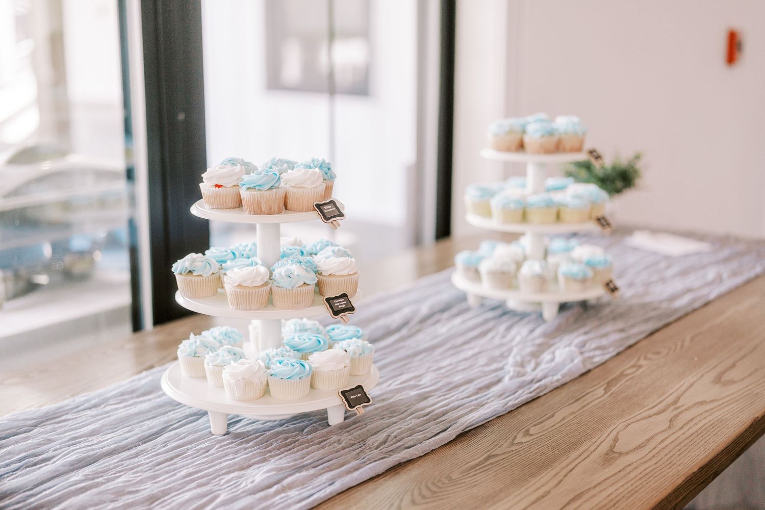 Elegant white and blue macarons displayed on rustic wooden tiered serving stands at a dessert table.