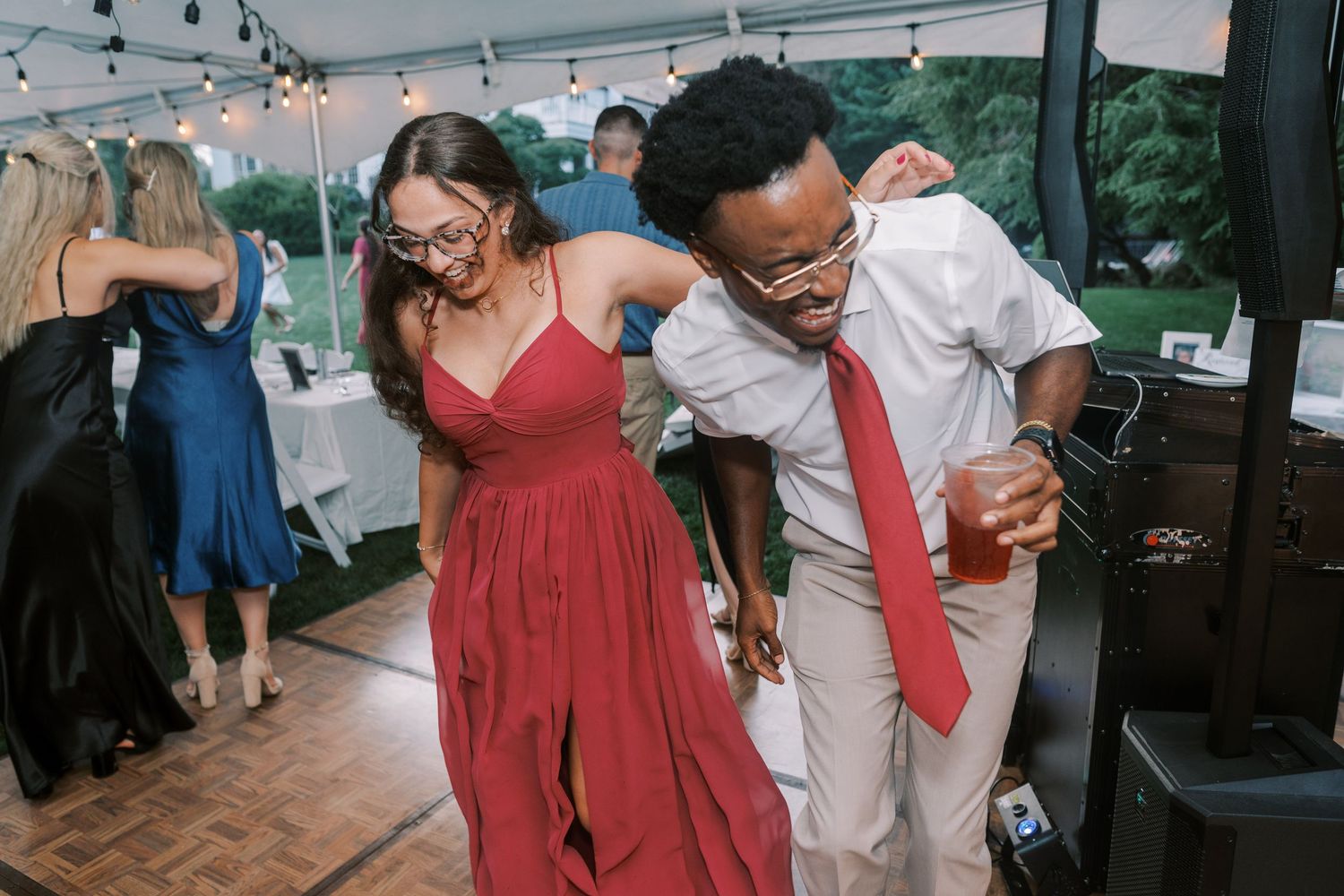Wedding guests dancing and laughing together at a reception under string lights.