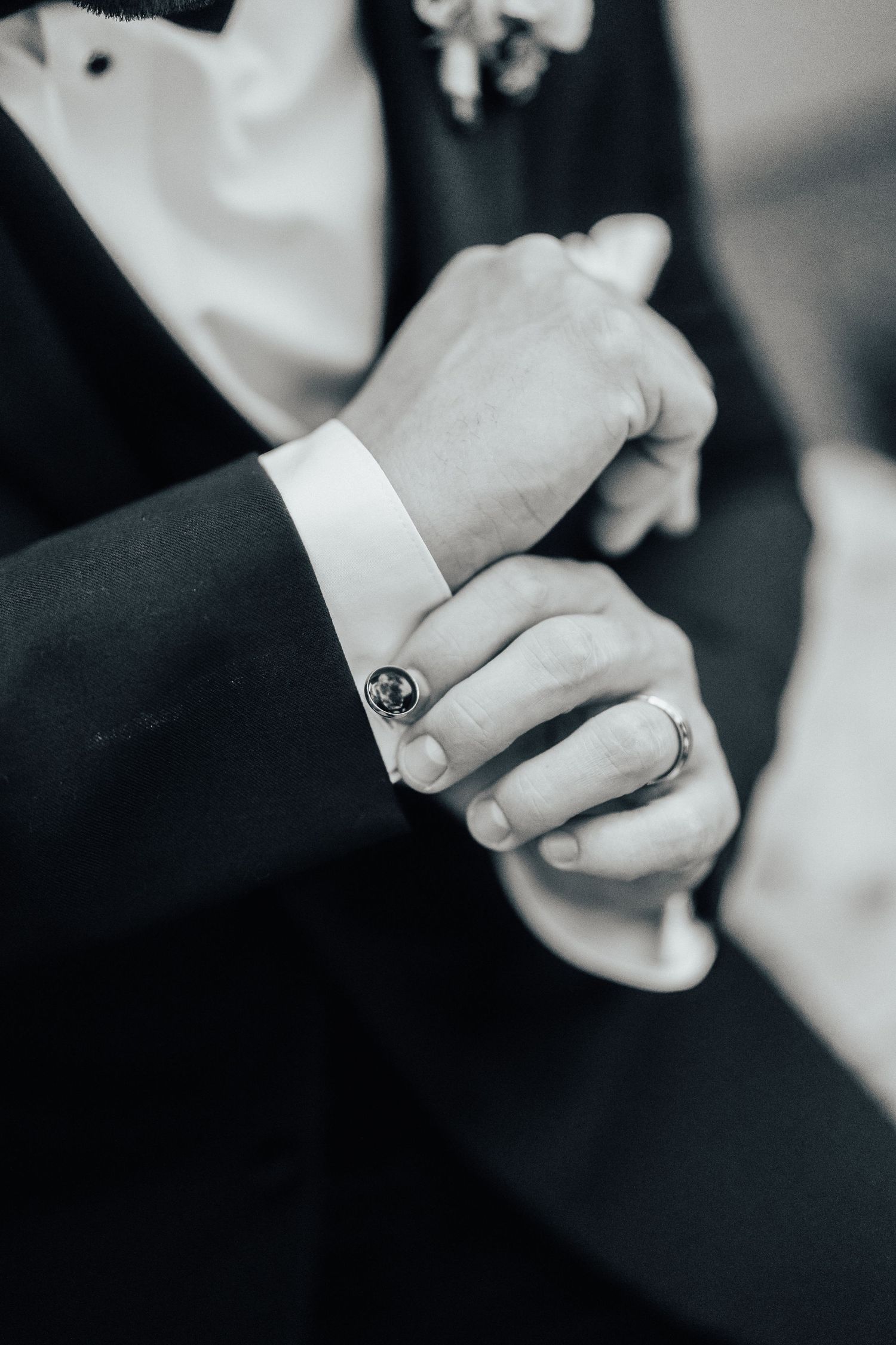 Close-up black and white photo of hands adjusting a cufflink on formal suit sleeve with white cuff.