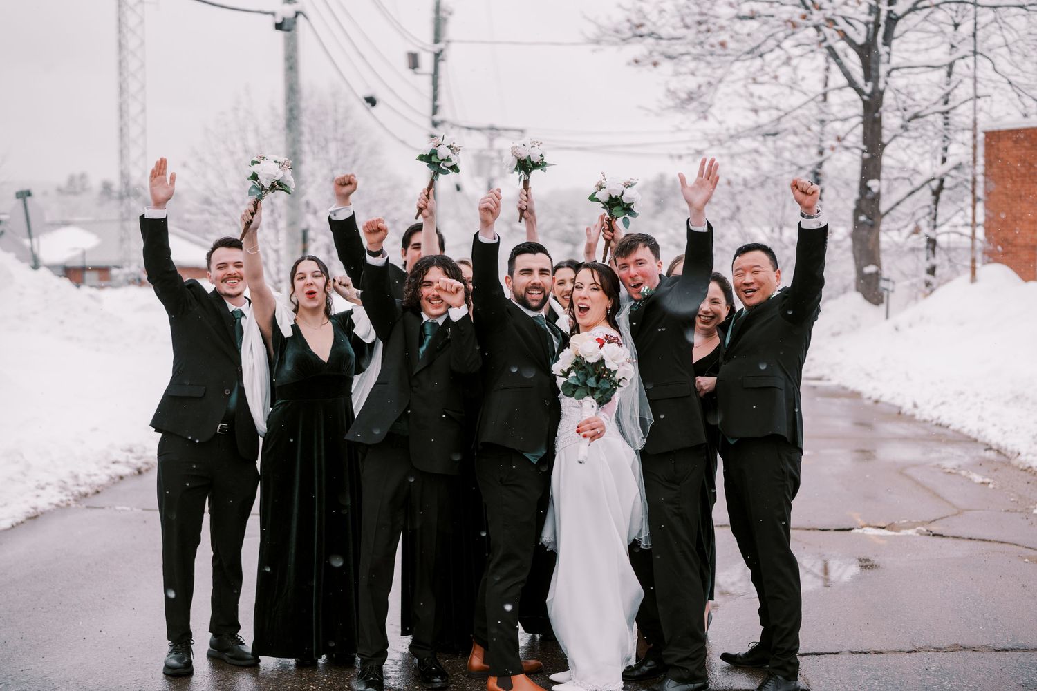 Wedding party celebrating with raised arms on snow-covered winter street.