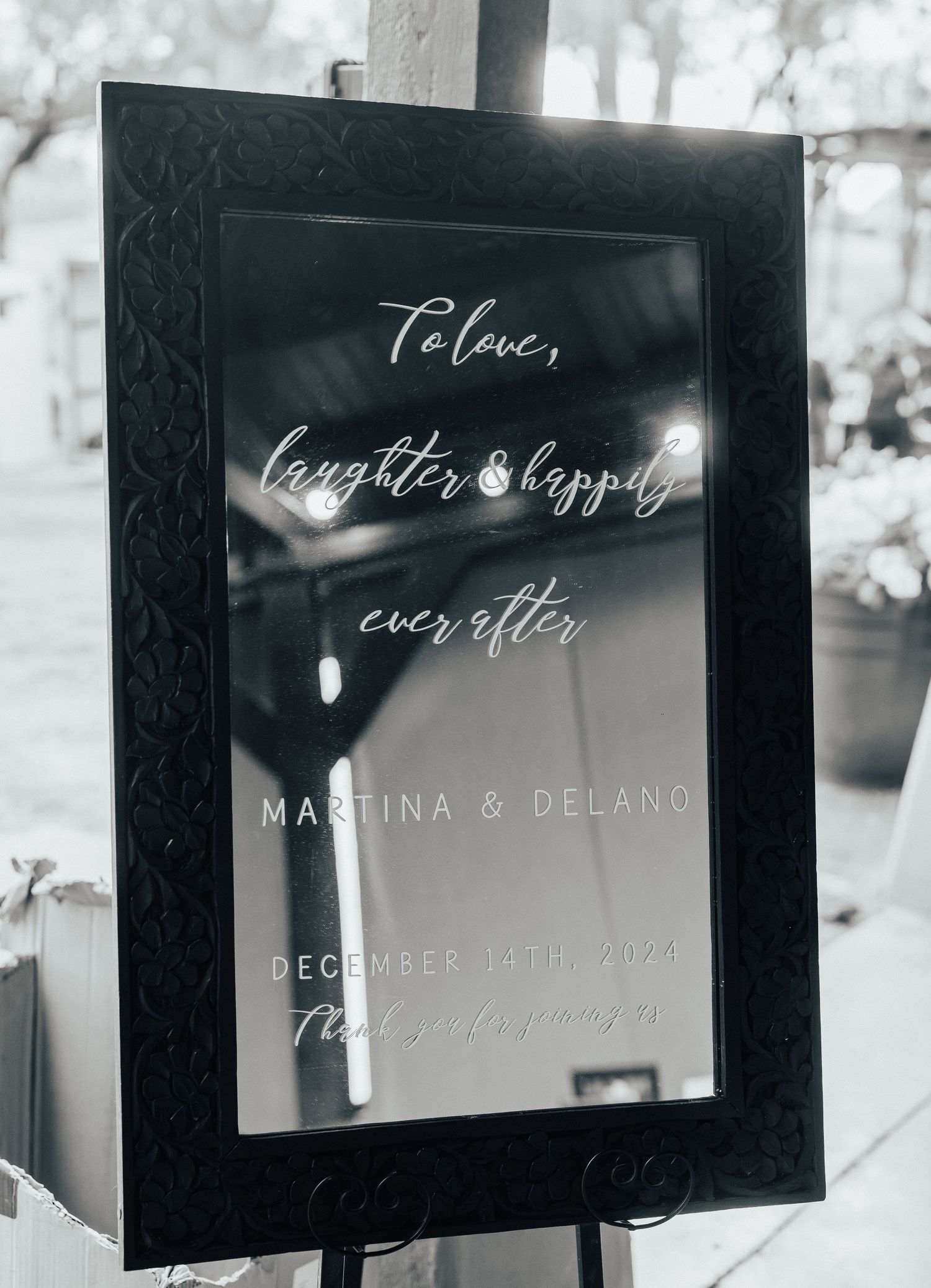 Black framed wedding welcome sign with white calligraphy text reading 'To love, laughter & happily ever after' in elegant style.