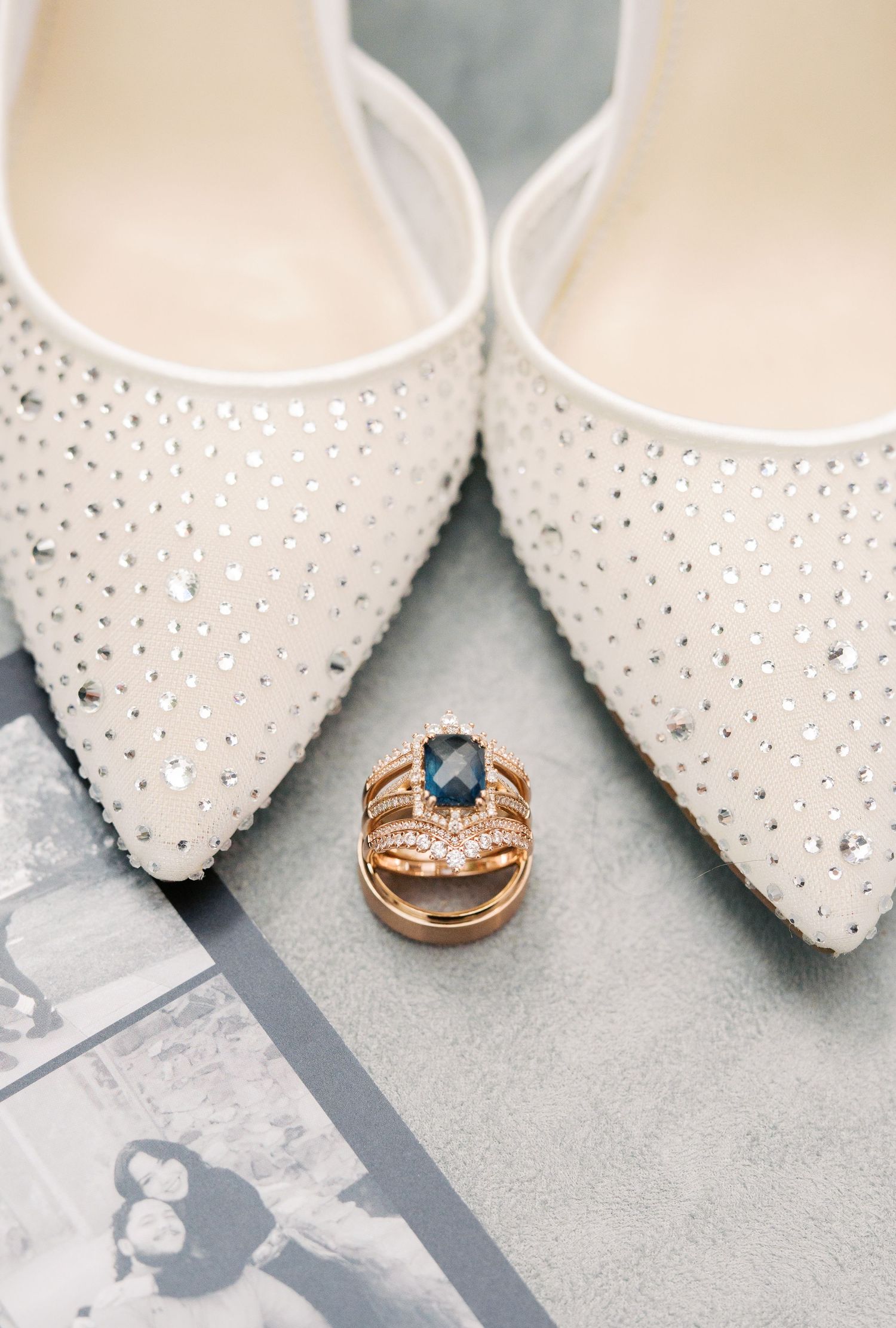 Sparkling bridal flats with crystal embellishments displayed with a blue sapphire and diamond rose gold wedding ring set.