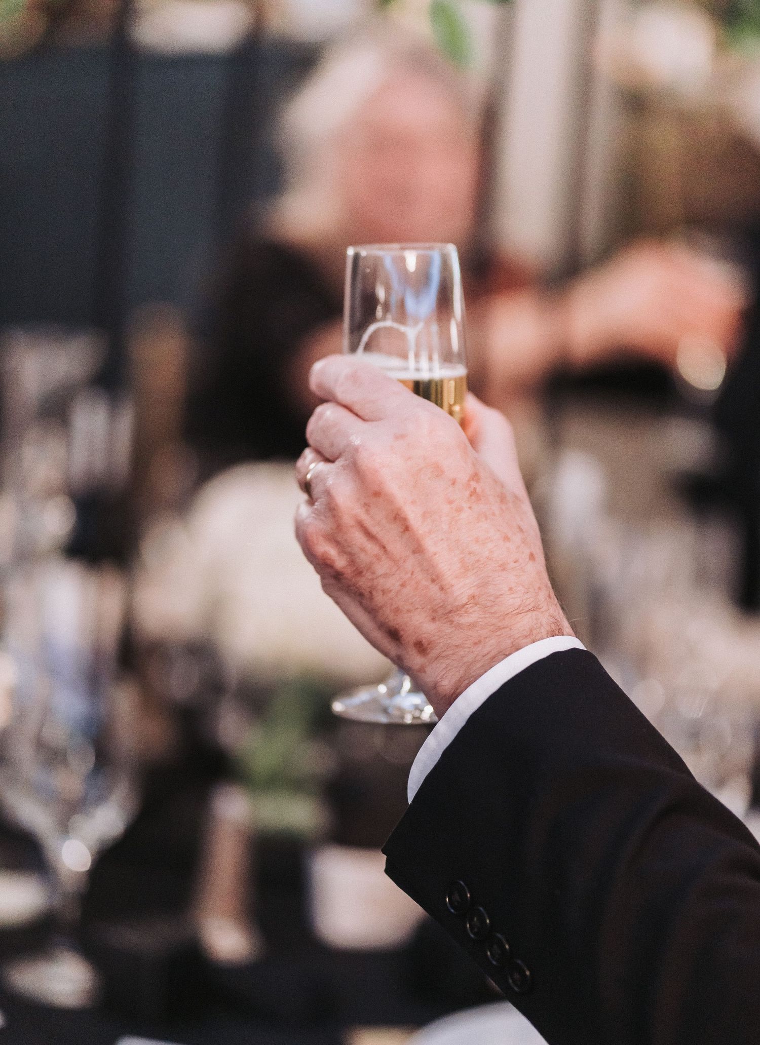 An elegantly dressed hand holding a champagne flute at a formal celebration.