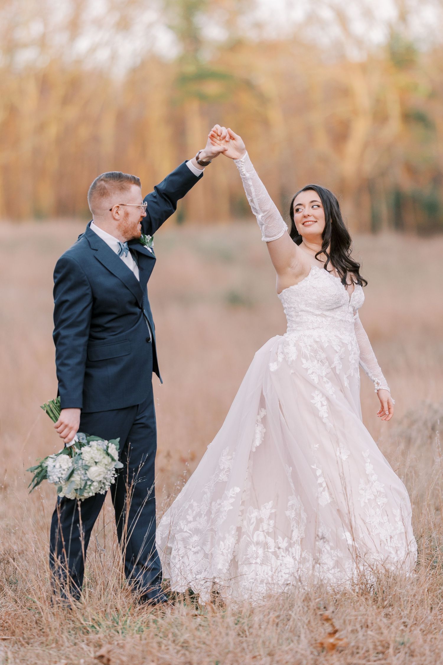 A couple celebrates their wedding day in a rustic field with tall grass and autumn colors as the bride holds a bouquet.