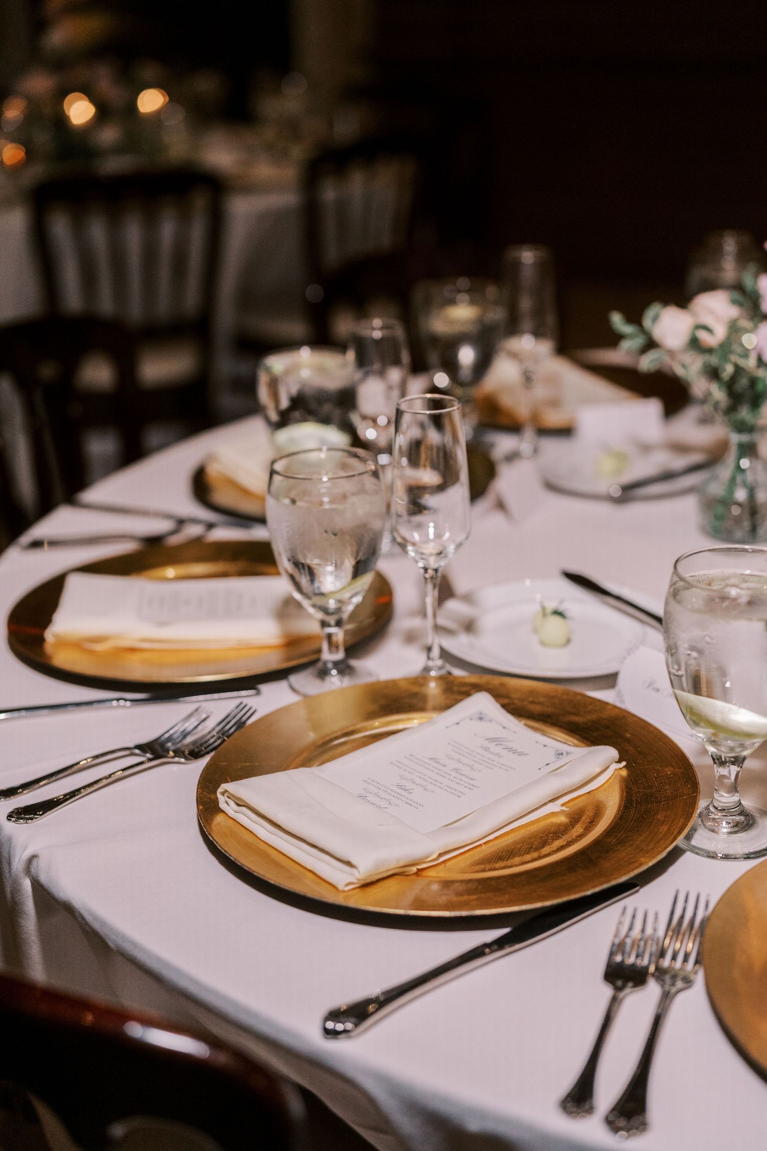 Elegant table settings with gold charger plates, white linens, and menu cards arranged for a formal dining event.