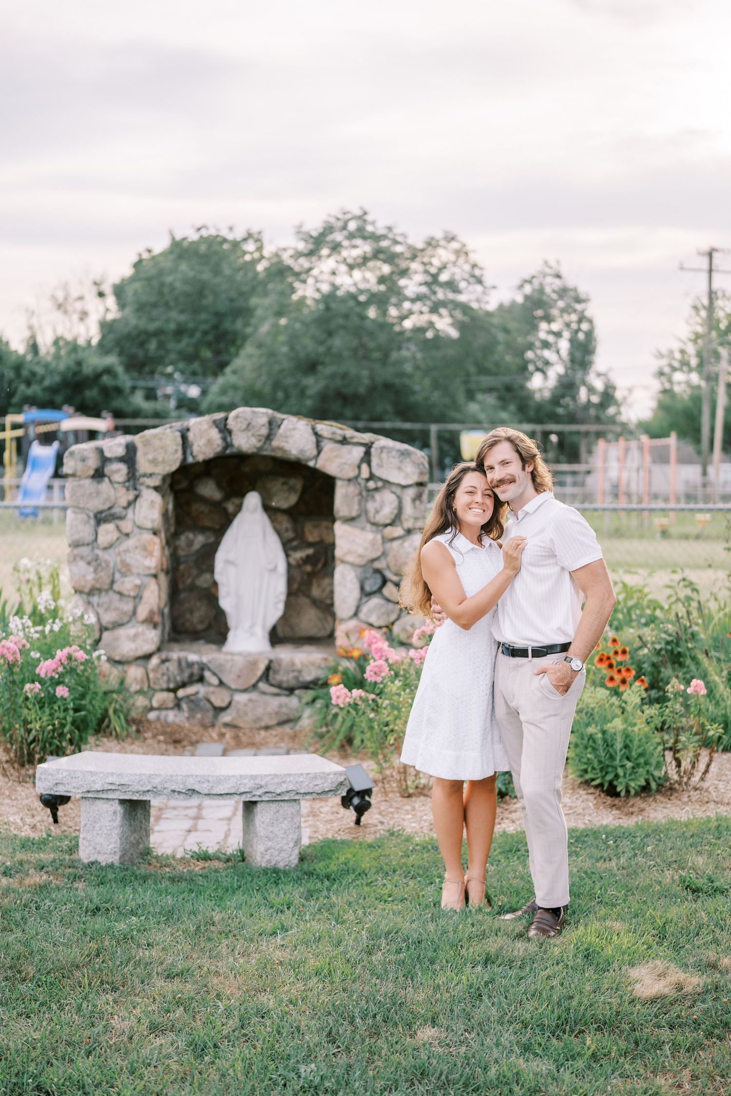 A romantic photoshoot in a garden with stone benches and pink flowers.