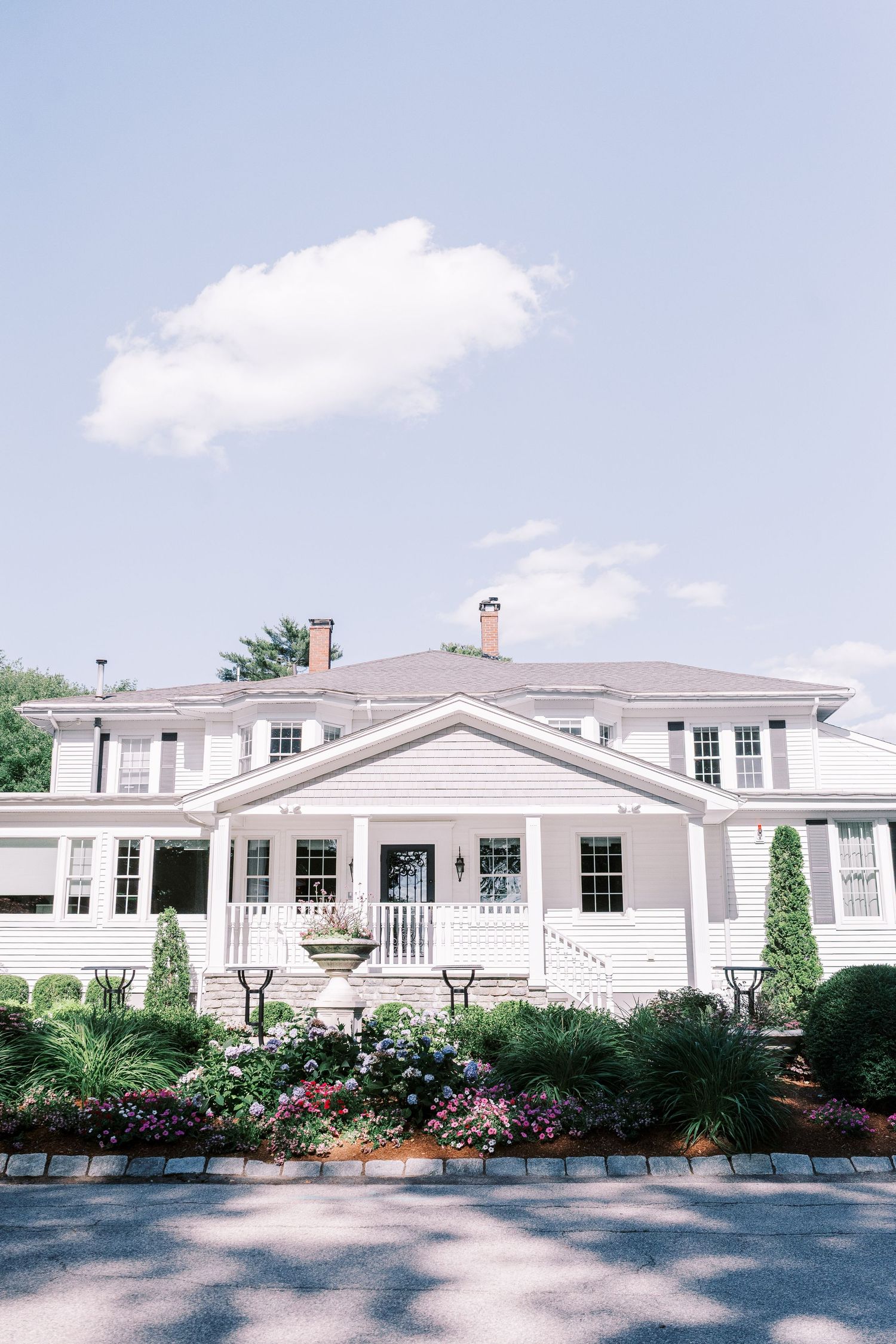 Elegant white colonial style house with symmetrical windows, front porch, and manicured garden landscaping against blue sky.